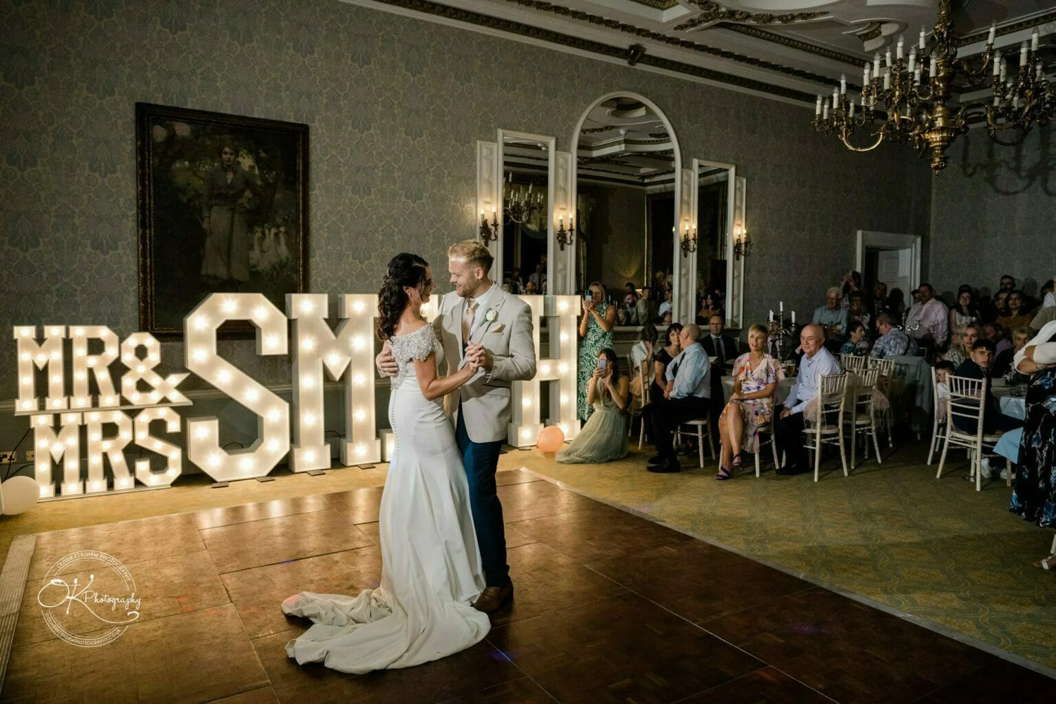Ettington Park Hotel Wedding Photography Bride and groom dancing in an elegant reception room with large illuminated "Mr & Mrs Smith" sign.