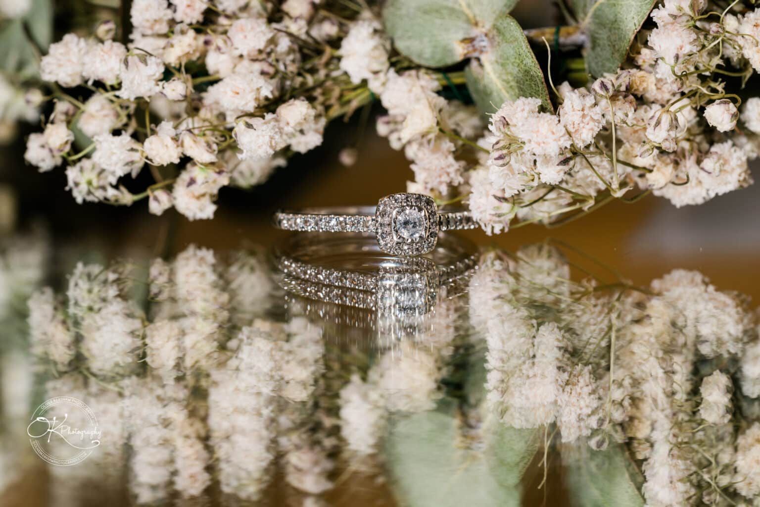 Mythe Barn Wedding photography A diamond ring reflected on a surface, accompanied by a bouquet of small white flowers.