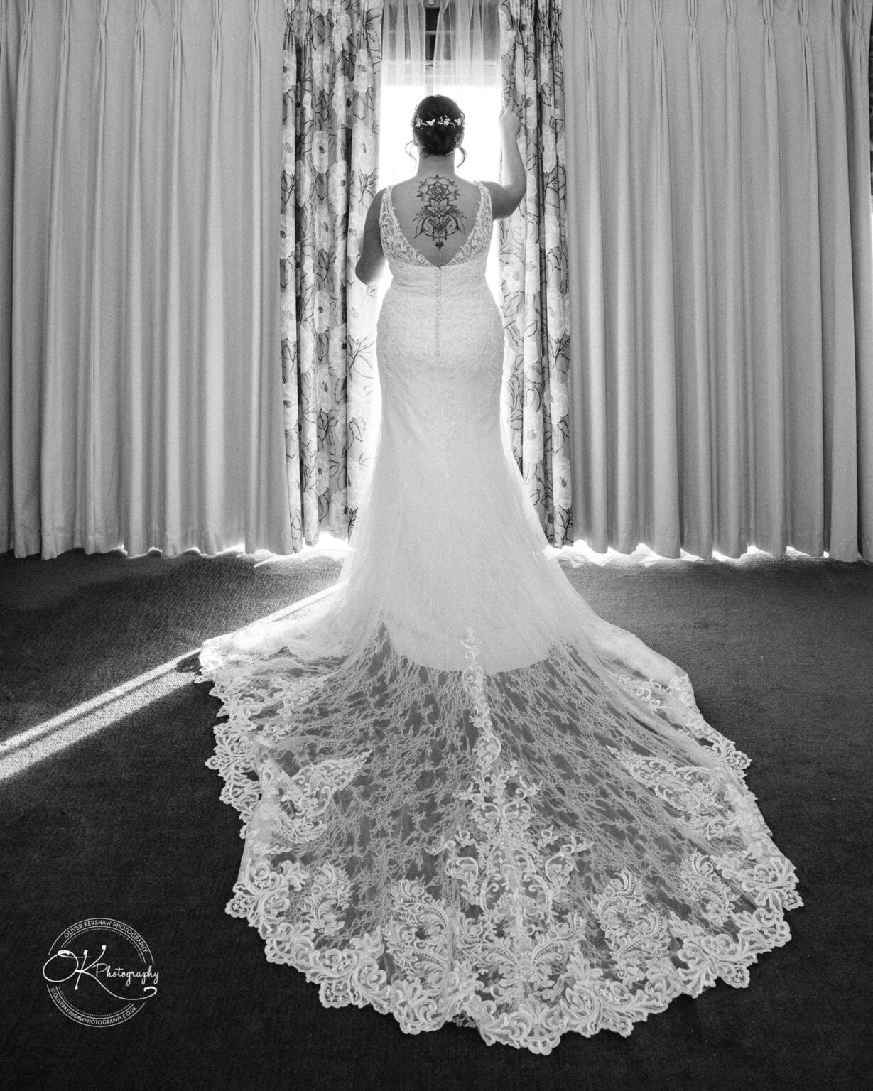 Mythe Barn Wedding photography A bride in a lace wedding dress and flower crown facing a window with curtains.