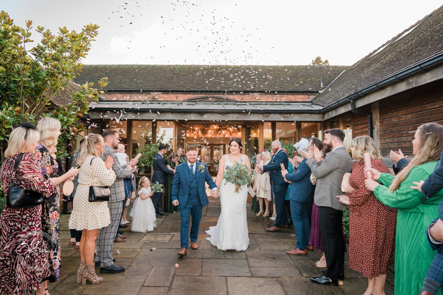 Mythe Barn Wedding photography A bride and groom walk down the aisle as guests throw confetti at a wedding ceremony at Mythe Barn.