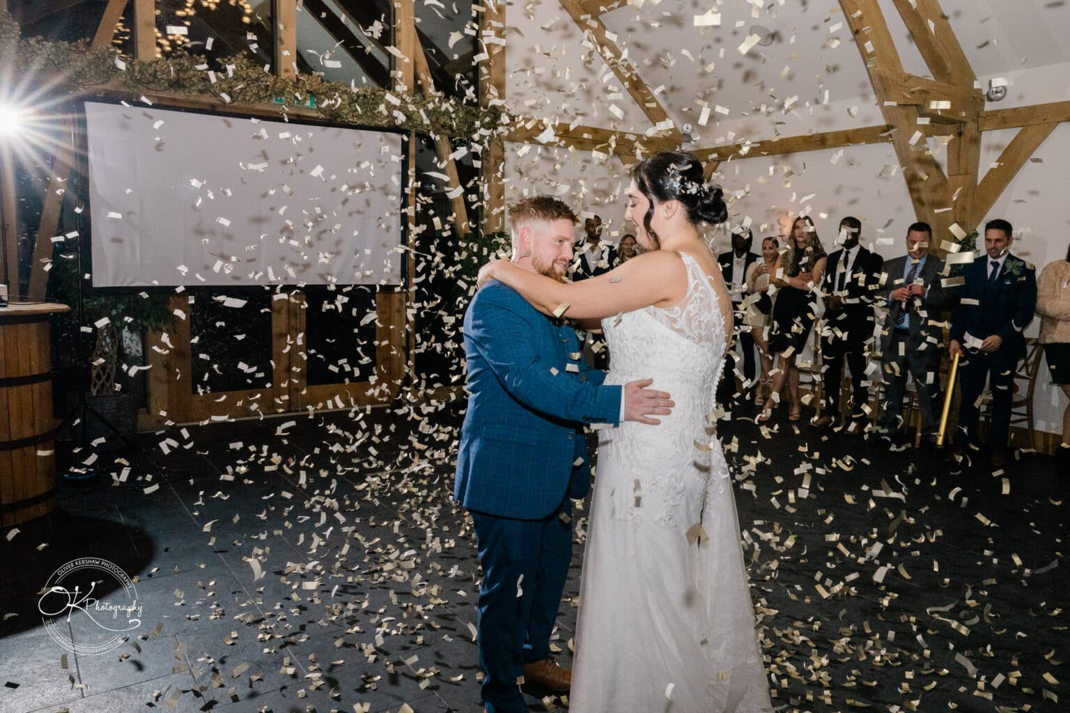 Mythe Barn Wedding photography A bride and groom share their first dance at a barn wedding, surrounded by fallen confetti and guests watching in the background.