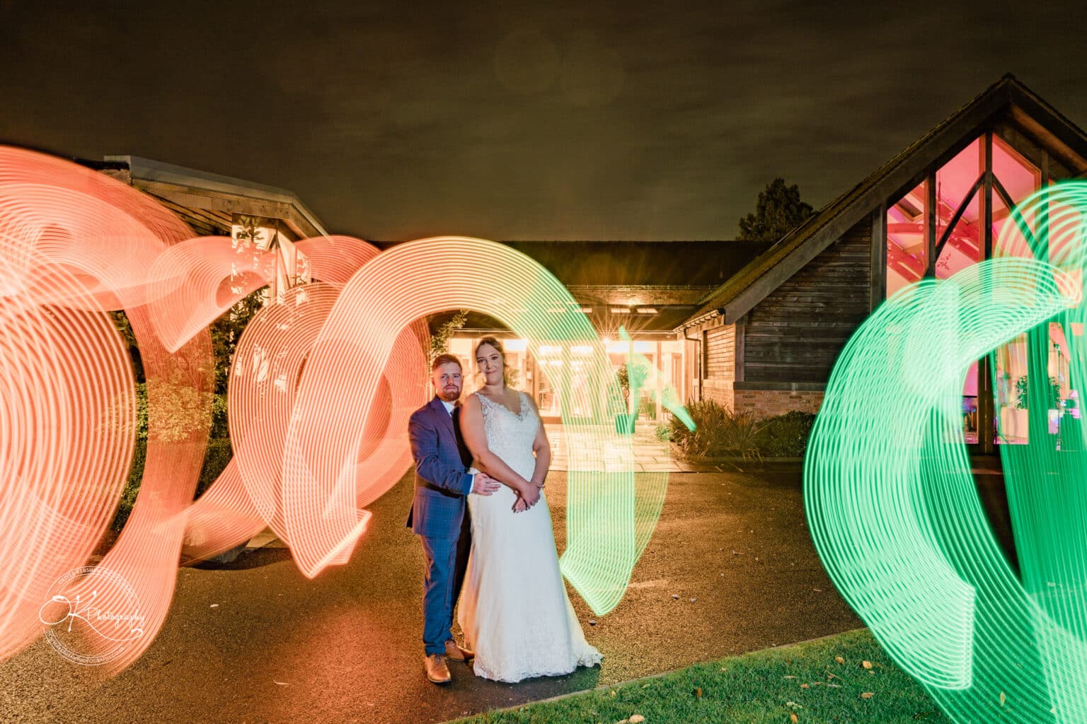 Mythe Barn Wedding photography Bride and groom standing outside a barn-style wedding venue, with colourful light trails surrounding them at night.