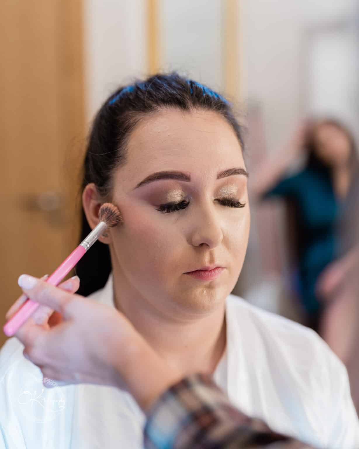Mythe Barn Wedding photography A woman with closed eyes having her makeup done with a brush.