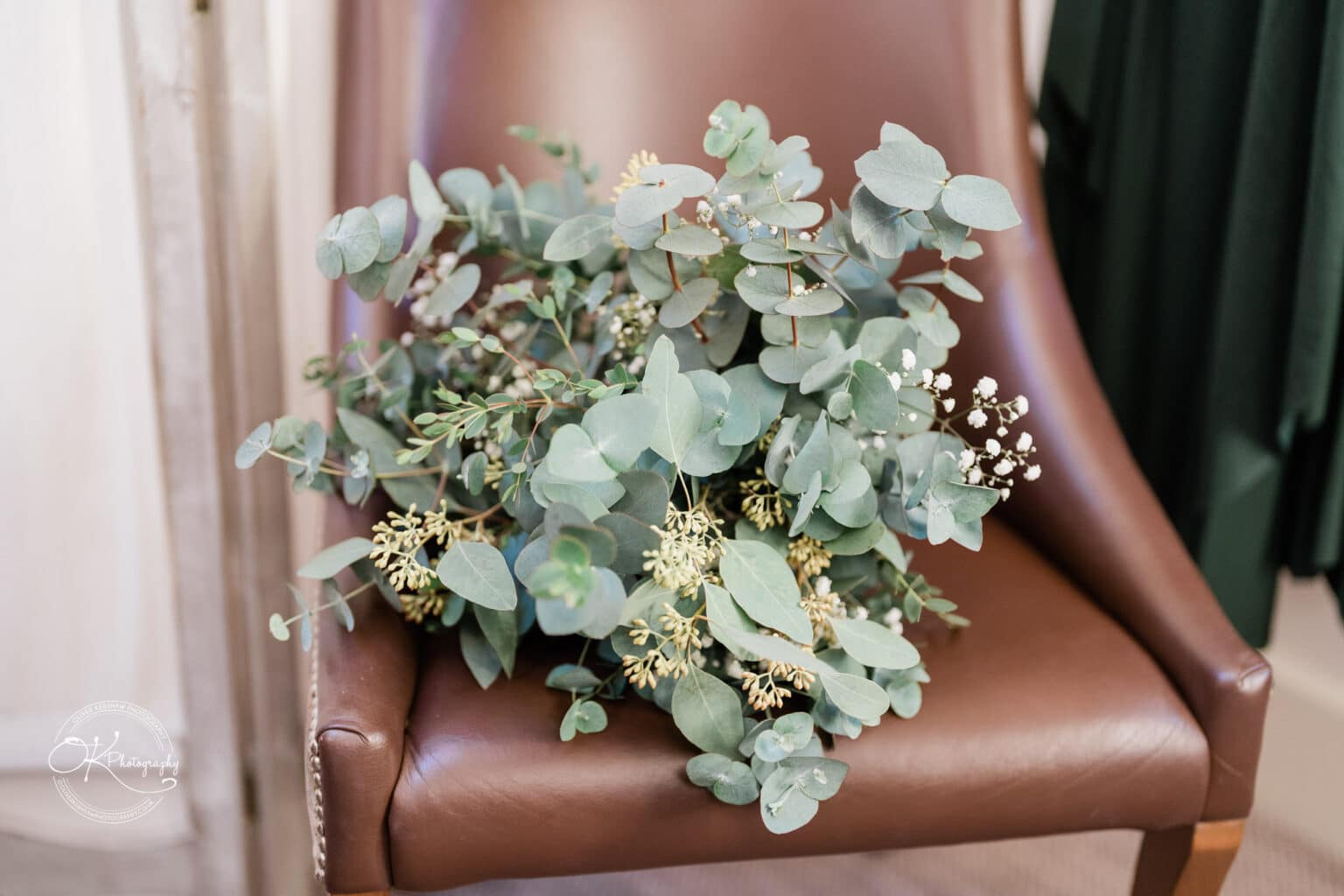 Mythe Barn Wedding photography A bouquet of greenery and small white flowers on a brown leather chair.