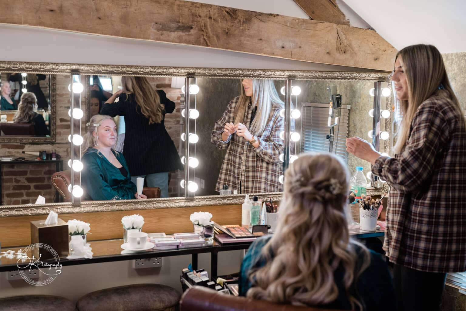 Mythe Barn Wedding photography Bride and bridesmaids getting ready in front of a large mirror surrounded by lights at Mythe Barn.