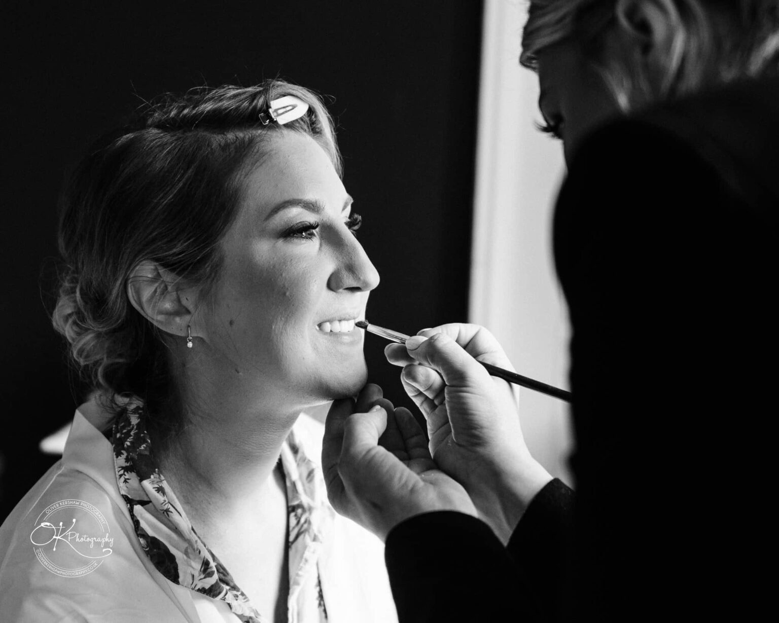 A black and white photo of a person having makeup applied by a makeup artist.