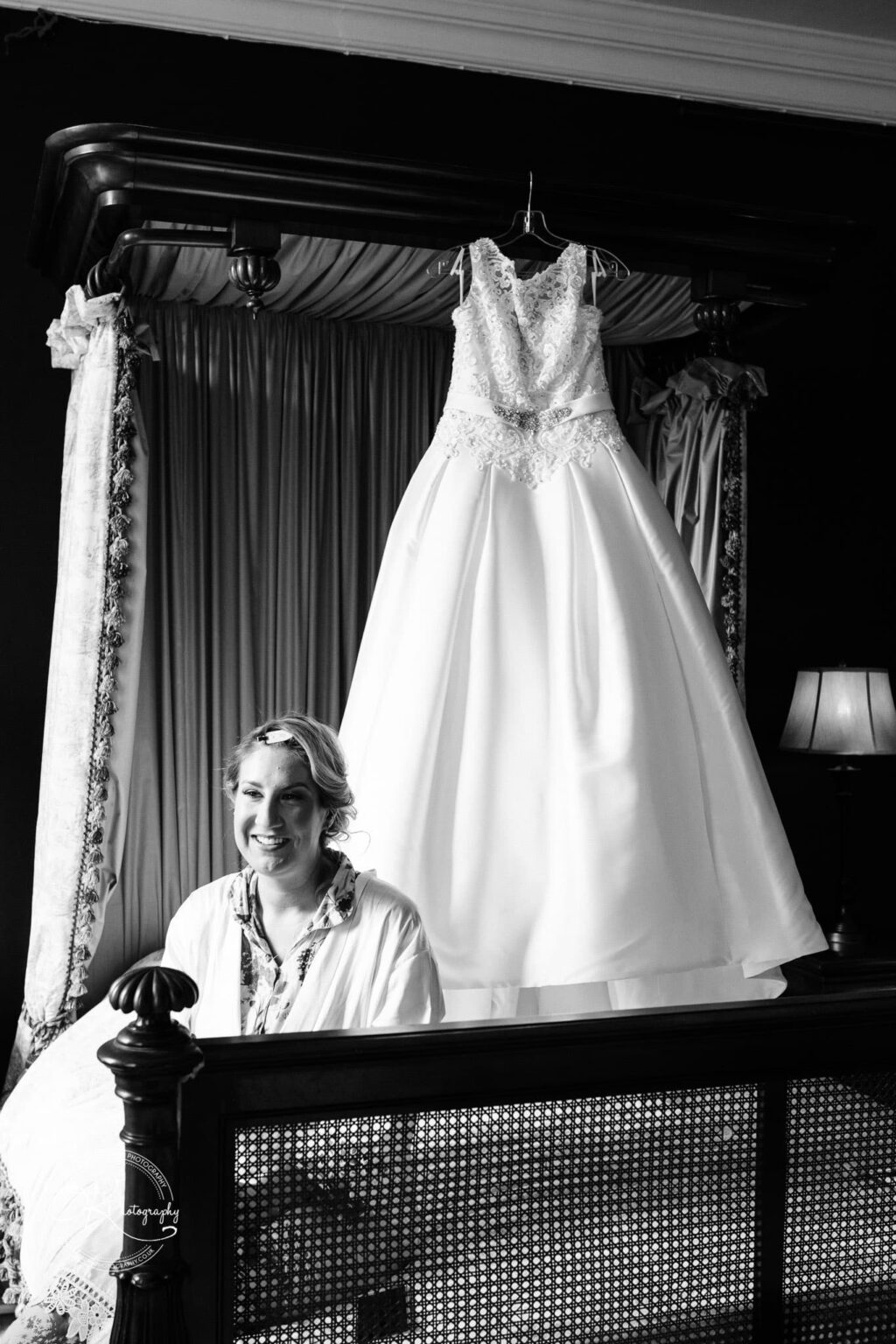 A bride getting ready in Prestwold Hall with her wedding dress hanging from a canopy bed in the background.