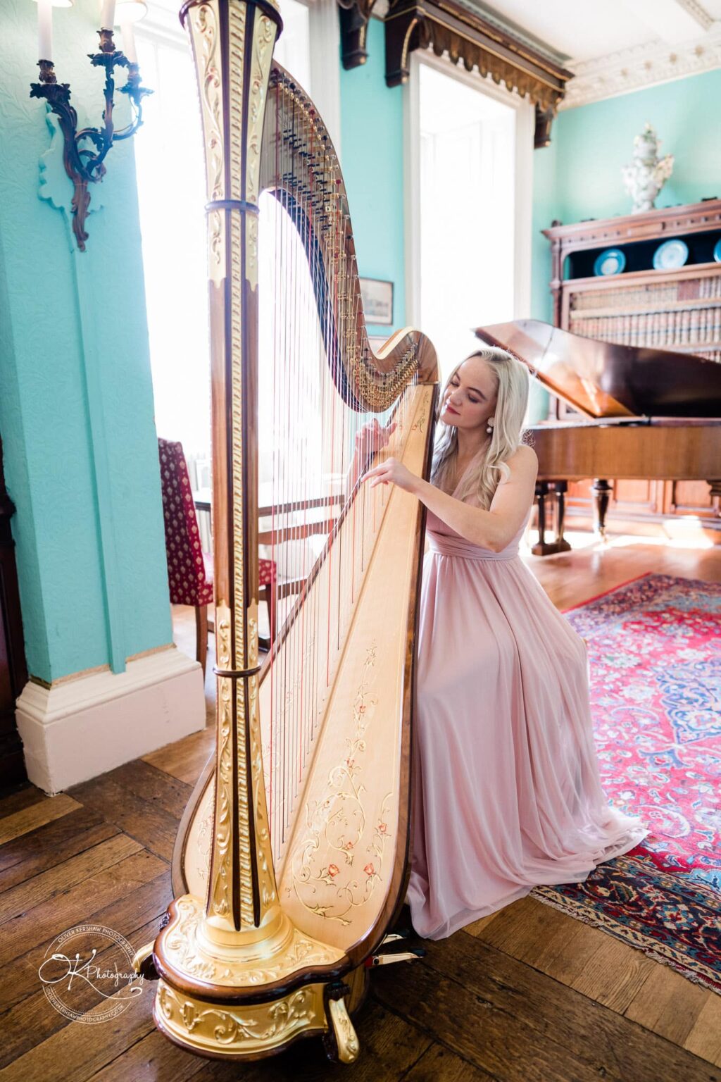 A woman playing a harp in an elegantly furnished room with a grand piano in the background.