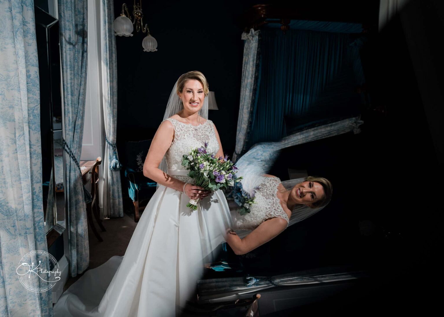 Bride in a white wedding dress holding a bouquet, standing in an elegantly decorated room with blue curtains and classical furnishings.