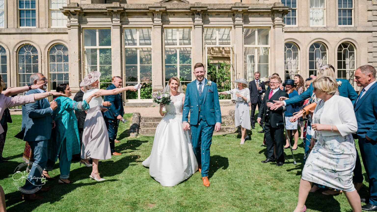 A bride and groom walk hand-in-hand as guests toss confetti outside Prestwold Hall.