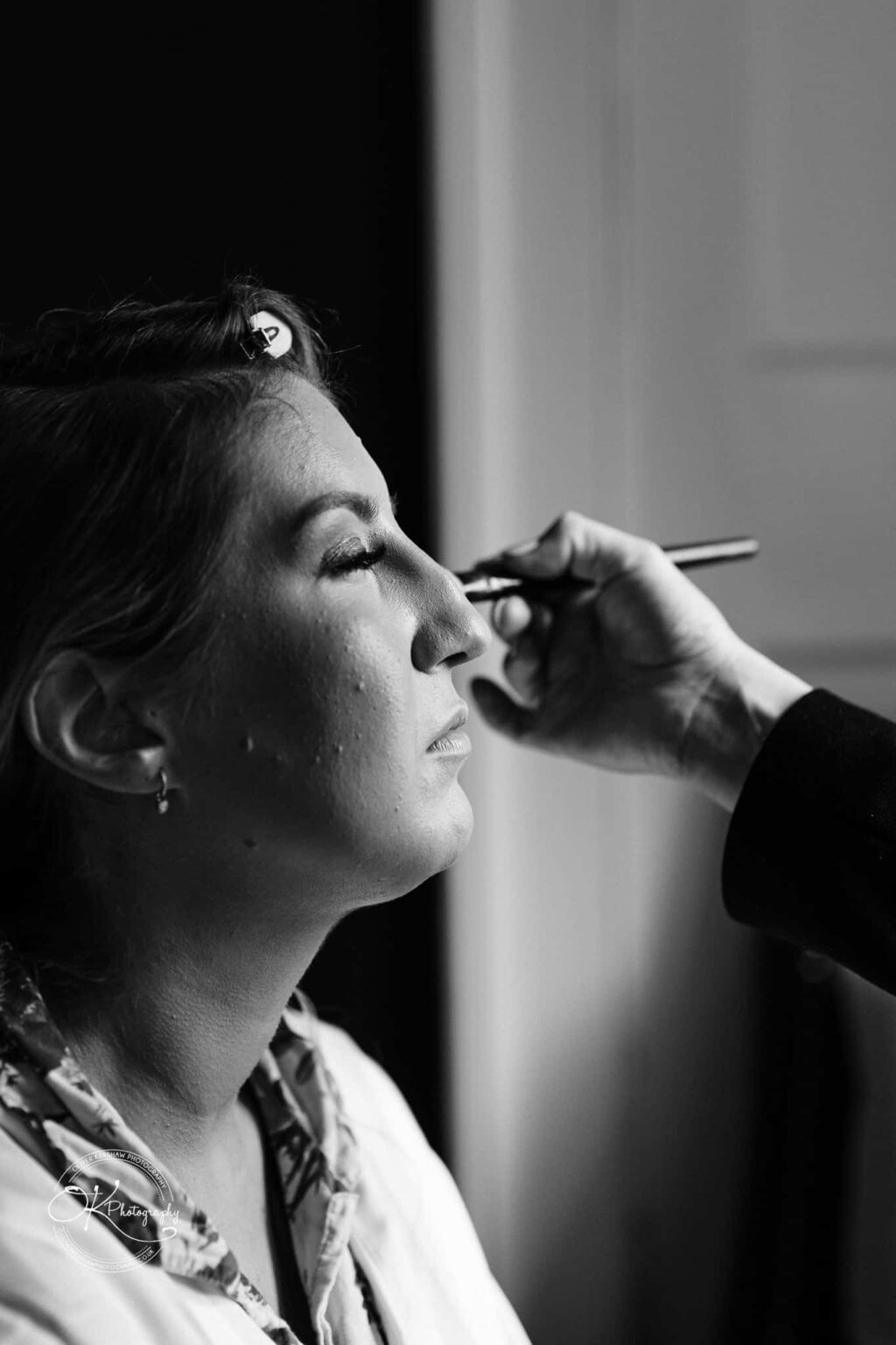 A person having makeup applied to their face, photographed in black and white.