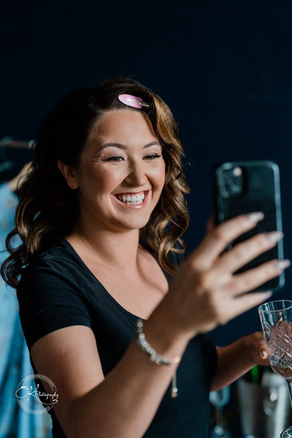 A smiling woman with a hair clip holding a smartphone and a glass.