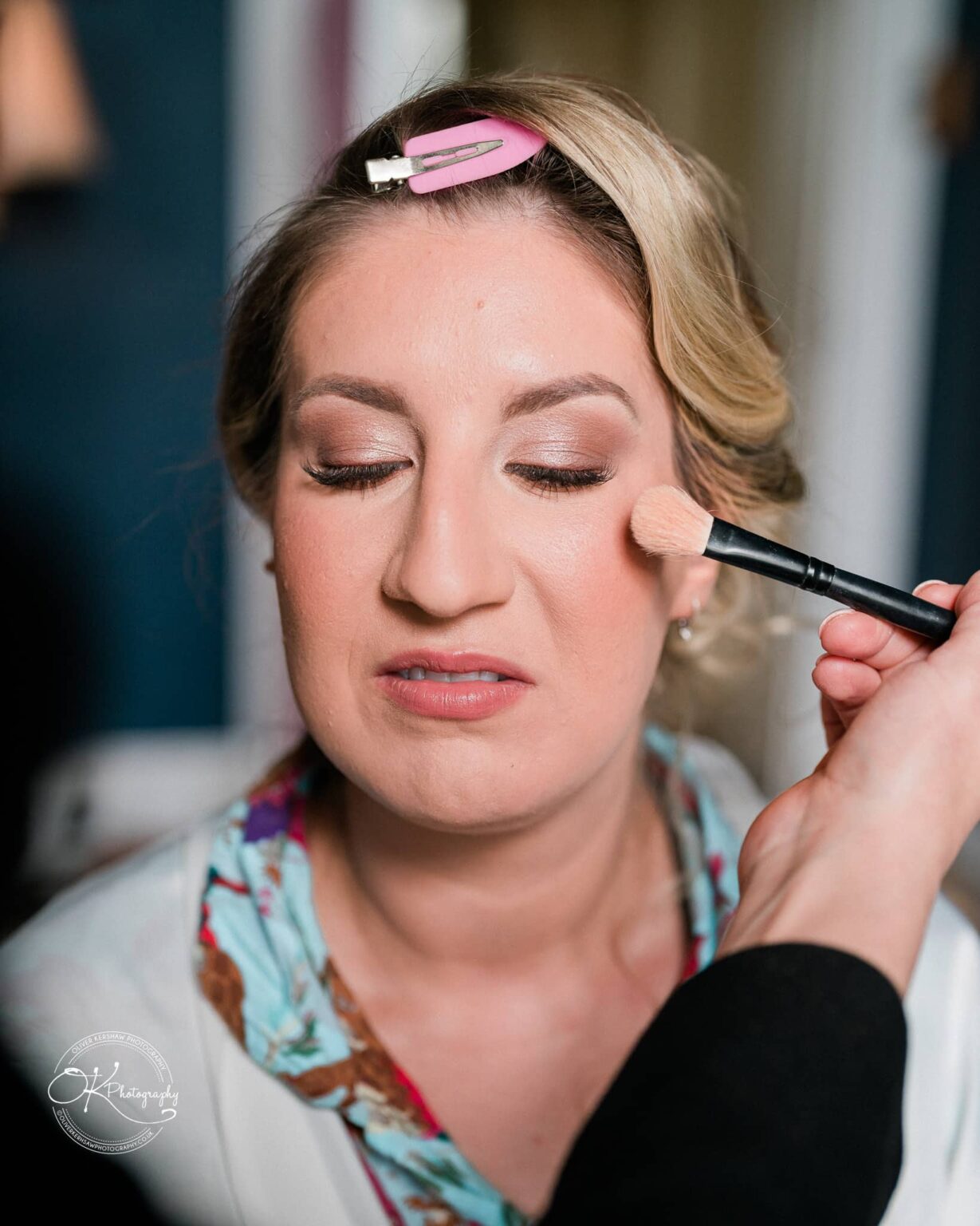 A woman having her makeup applied with a brush, hair held back with a clip.