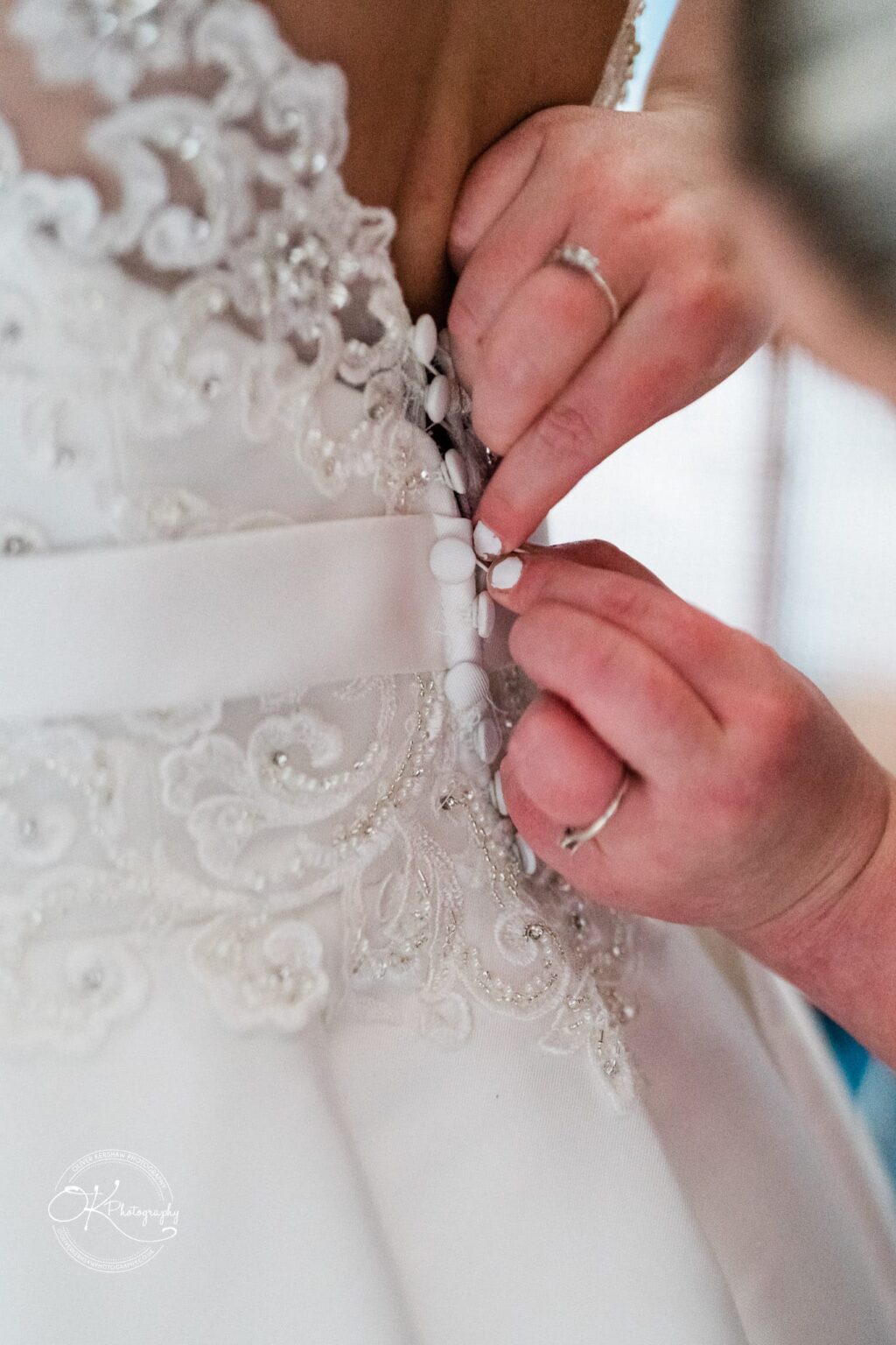Close-up of a person's hands fastening buttons on the back of an intricate lace wedding dress.