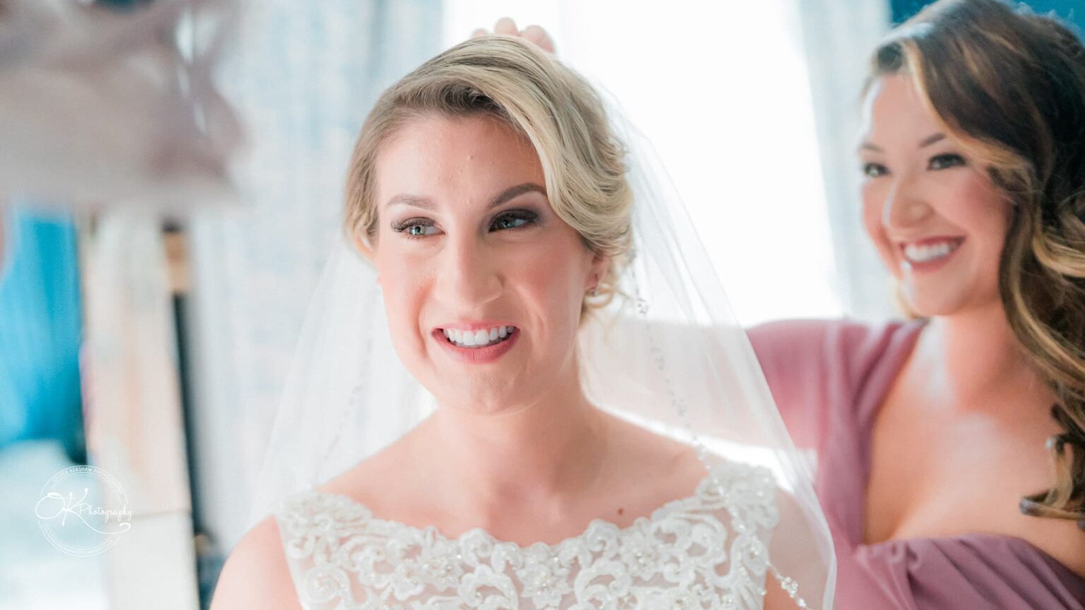 A bride smiling while a bridesmaid adjusts her veil.