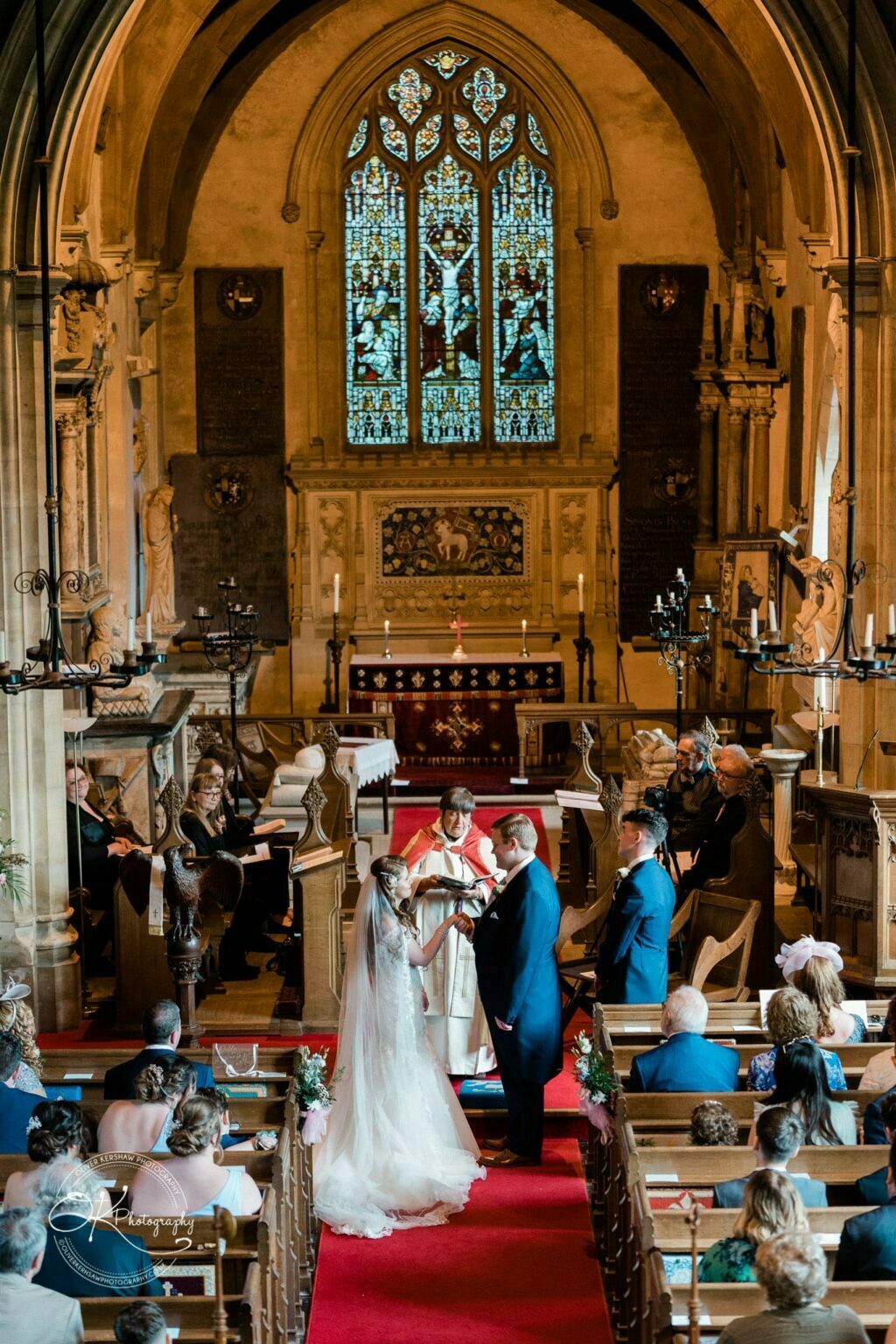 Prestwold Hall Wedding Photography A wedding ceremony taking place inside a historic chapel, with stained glass windows, an altar, and guests seated in pews.