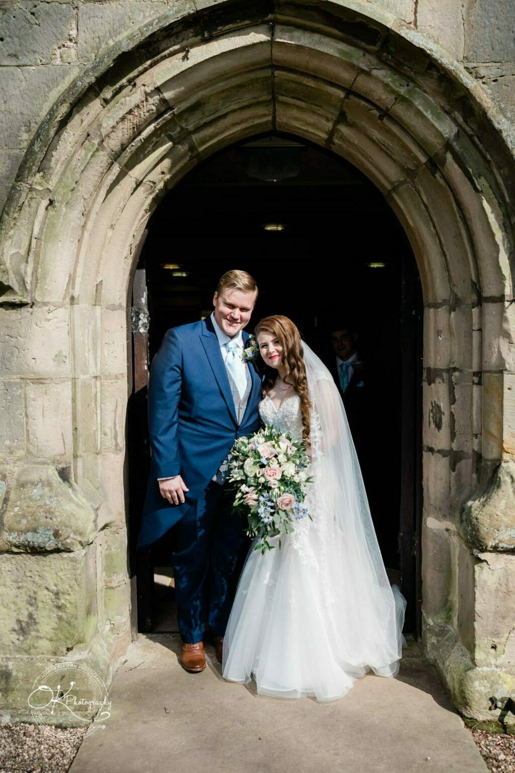 Prestwold Hall Wedding Photography A bride and groom standing under the stone archway of a church entrance.
