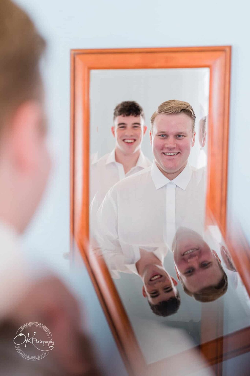 Prestwold Hall Wedding Photography Two men in white shirts smiling into a mirror, with their reflections visible.