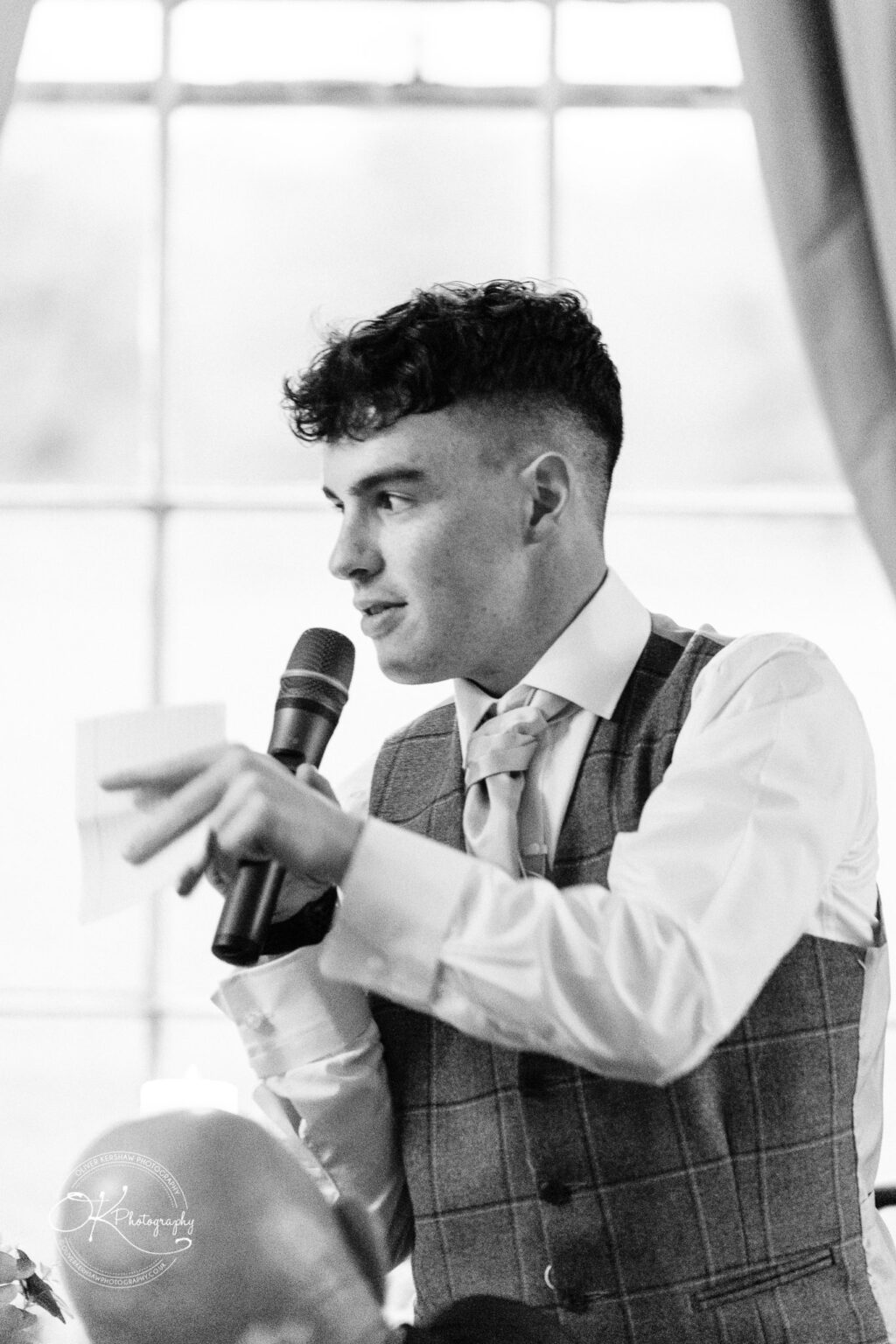 Prestwold Hall Wedding Photography A man in formal attire giving a speech and holding a microphone.