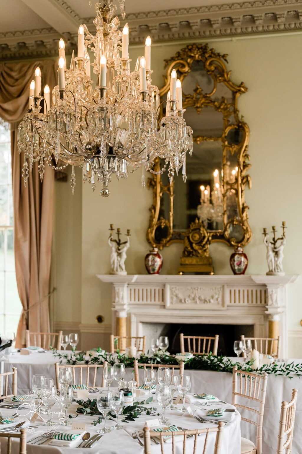Elegant ballroom interior at Prestwold Hall with a grand chandelier, ornate mirror, fireplace, and beautifully set dining tables.