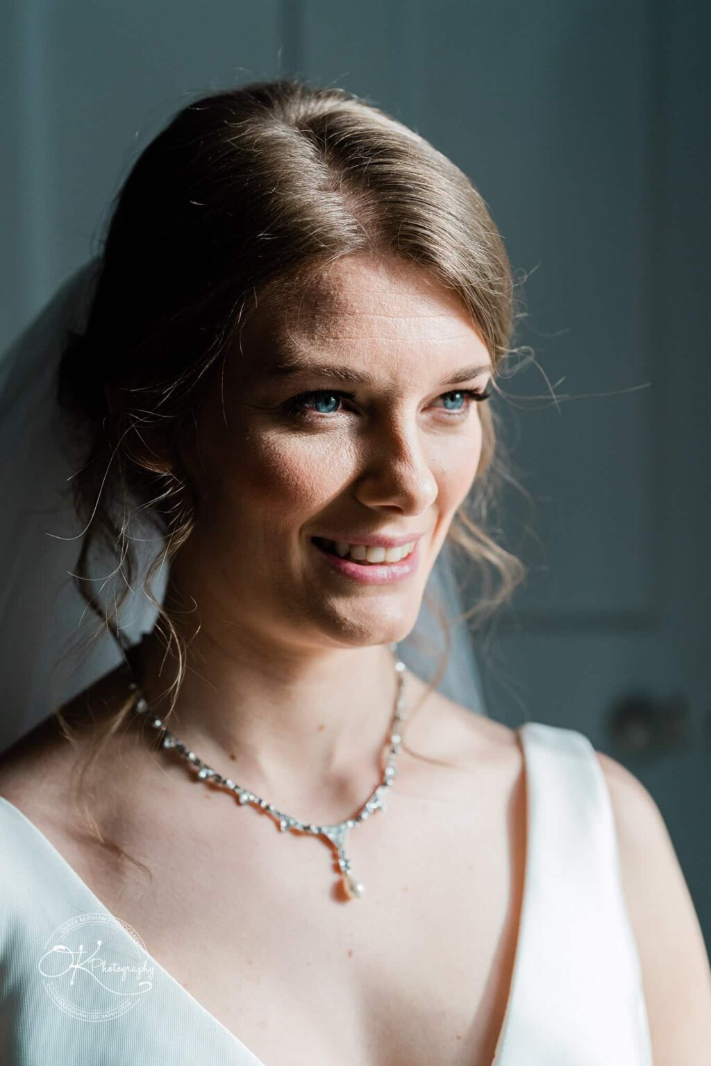 A smiling bride in a white wedding dress with a veil and a pearl necklace.