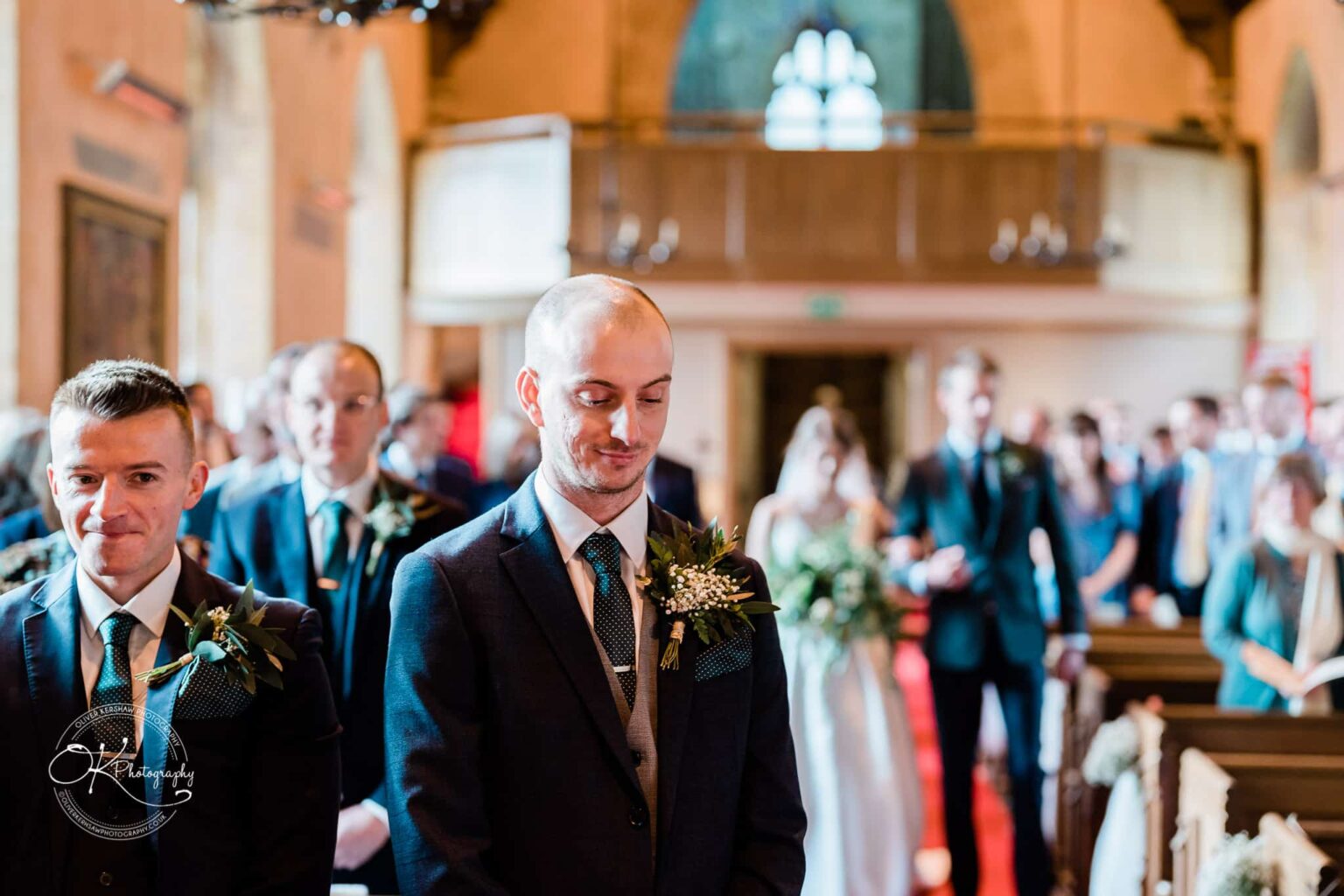 Groom and best man standing at the altar in a church, with guests in the background.