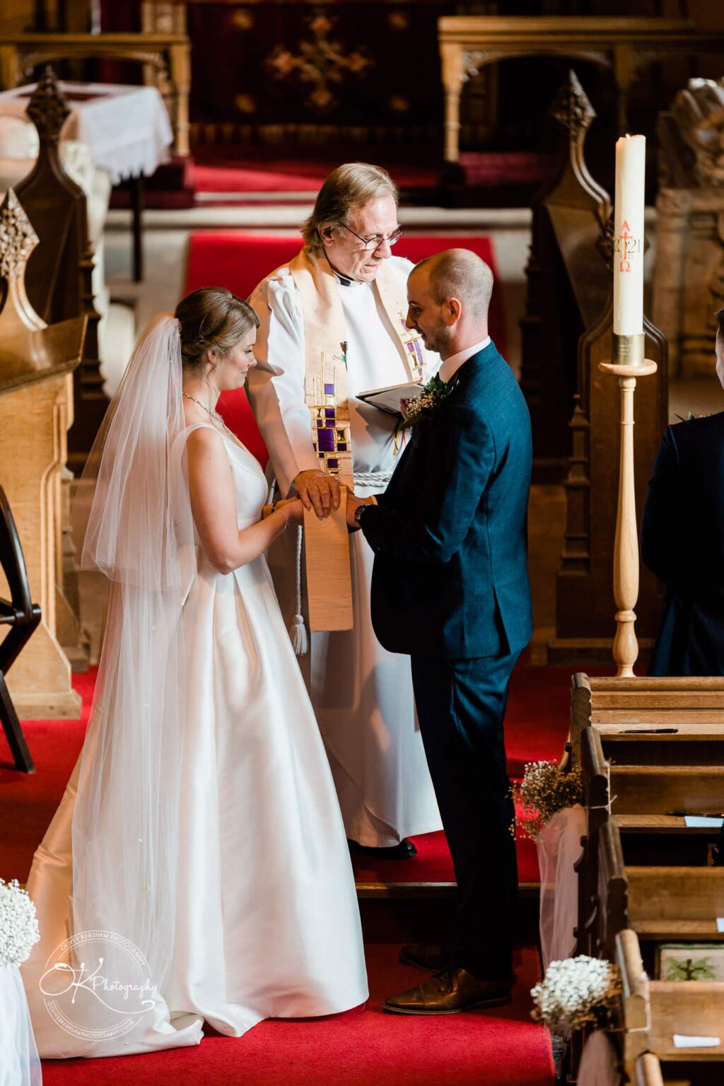 A bride and groom exchange vows in a church ceremony with a priest officiating.