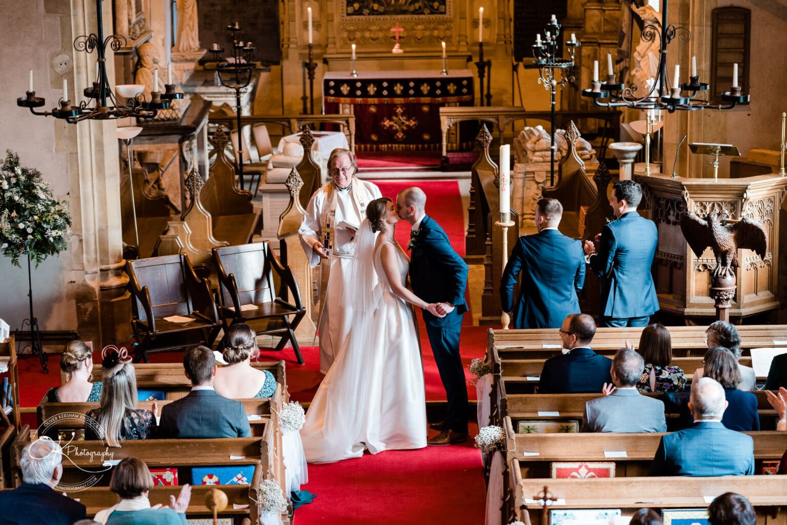 Wedding ceremony inside a church, with a couple kissing at the altar, surrounded by guests and a priest.