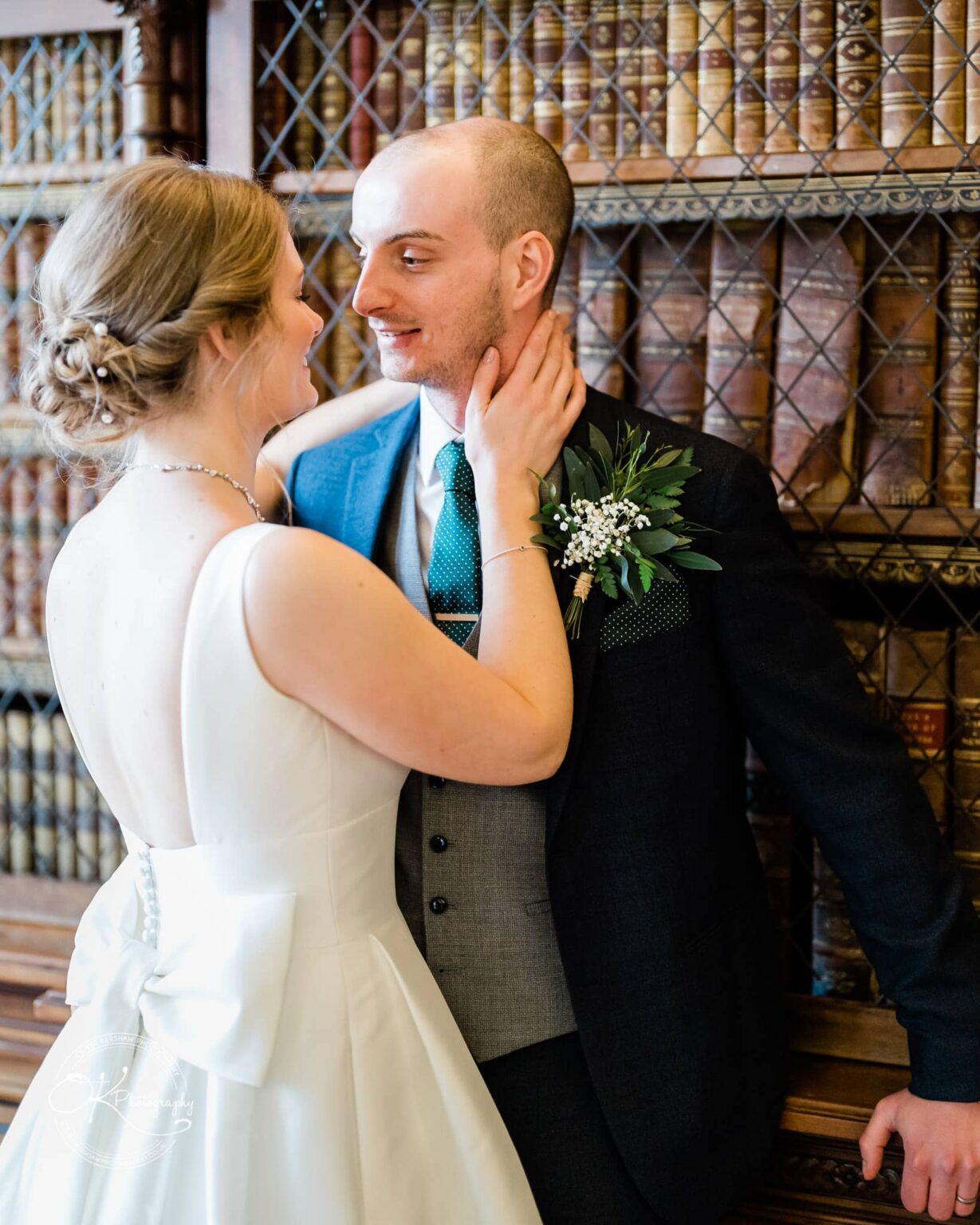 A bride and groom embracing in front of a bookcase at Prestwold Hall.