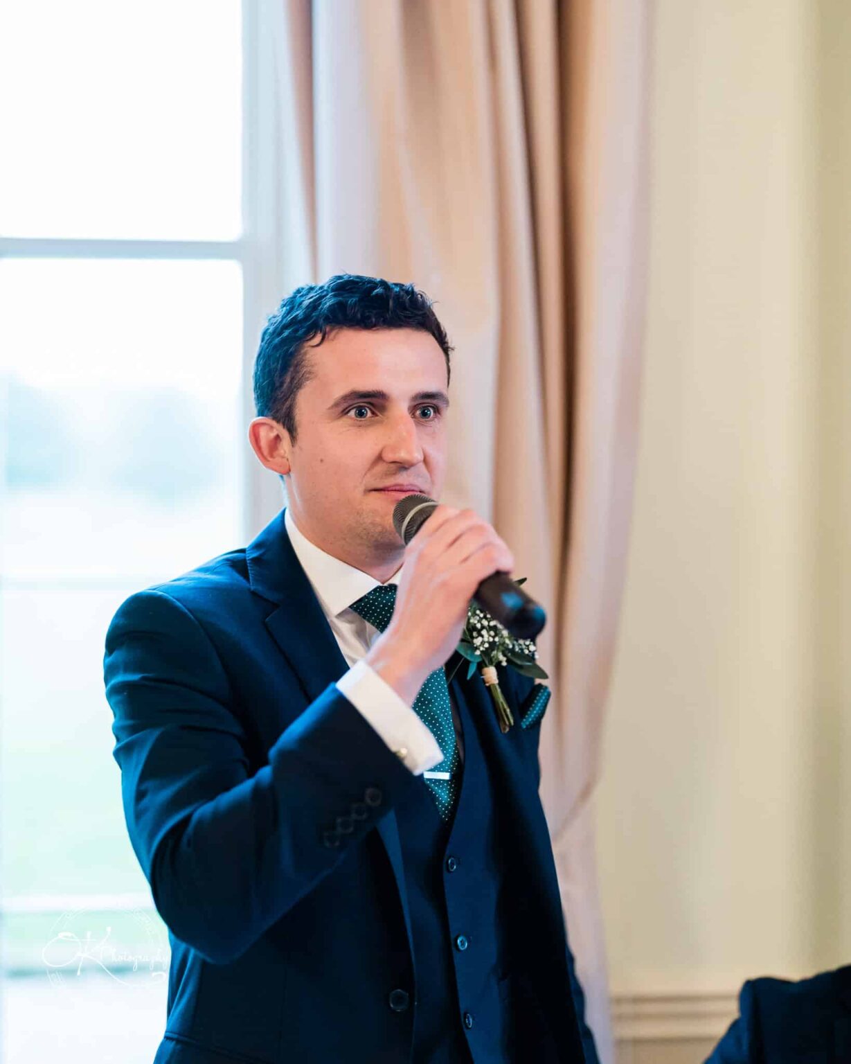 Man in a blue suit giving a speech with a microphone indoors.
