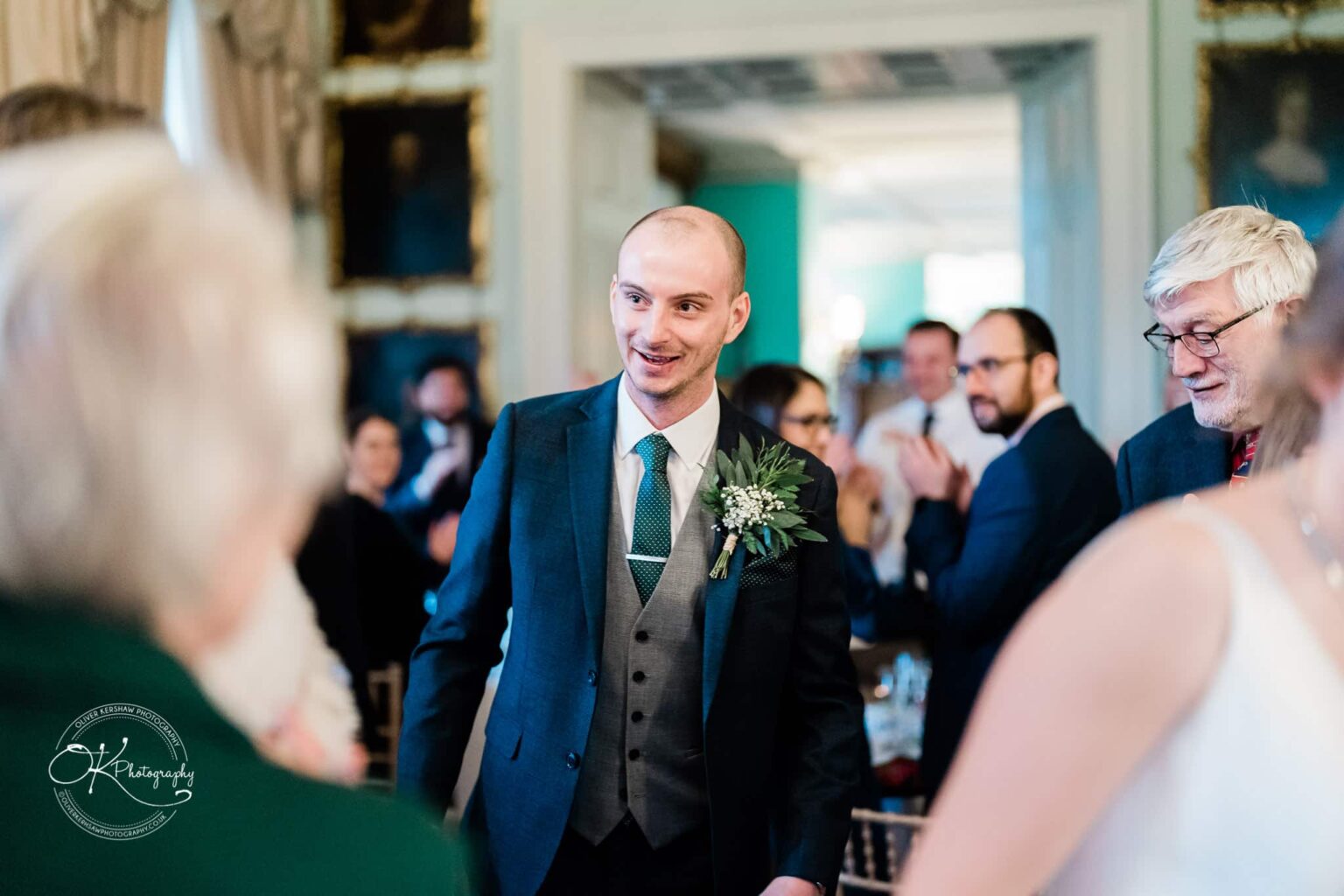 A man in a suit with a boutonniere smiles while surrounded by people at Prestwold Hall.