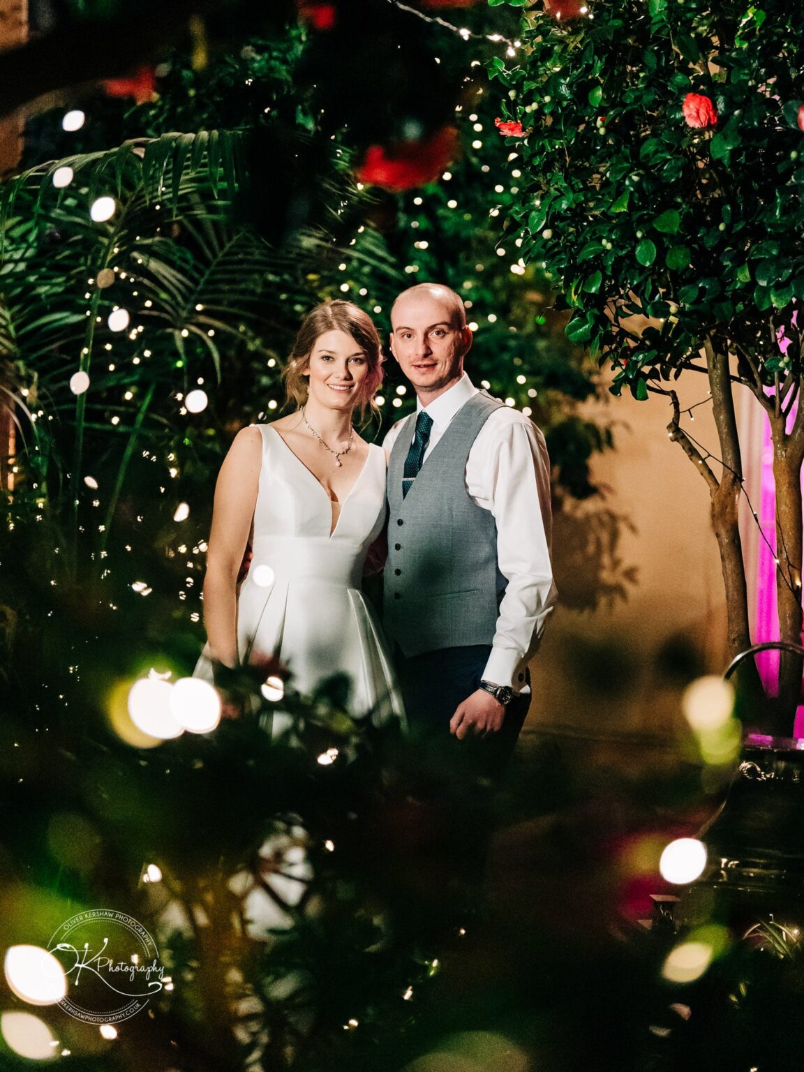 A couple standing together in a decorated garden with fairy lights and foliage.