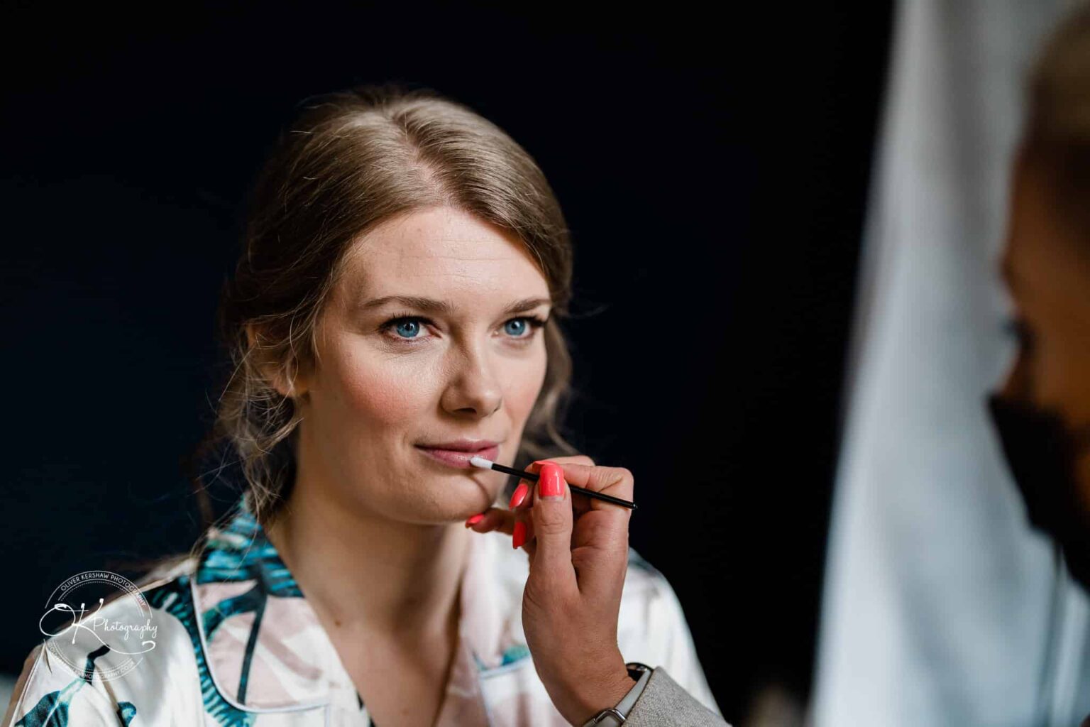 A woman having her makeup applied with a brush on her lips.