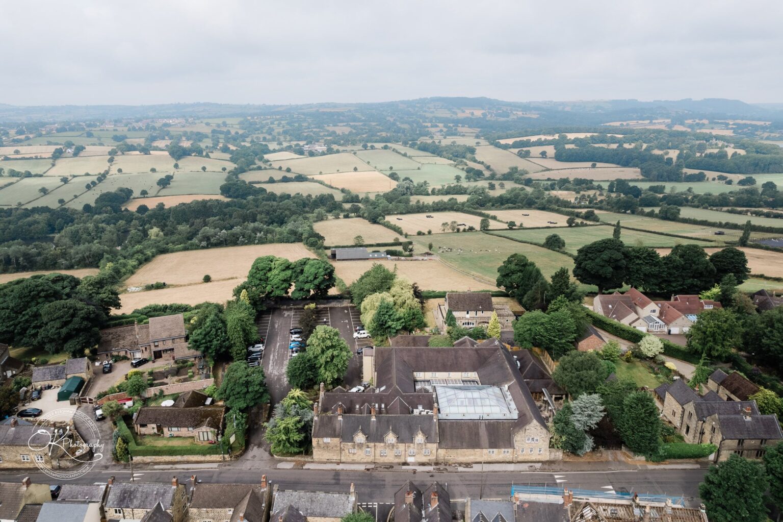 Santos Higham Farm Wedding Photography Aerial view of Santos Higham Farm, showing a cluster of buildings, a car park, and surrounding fields and countryside.