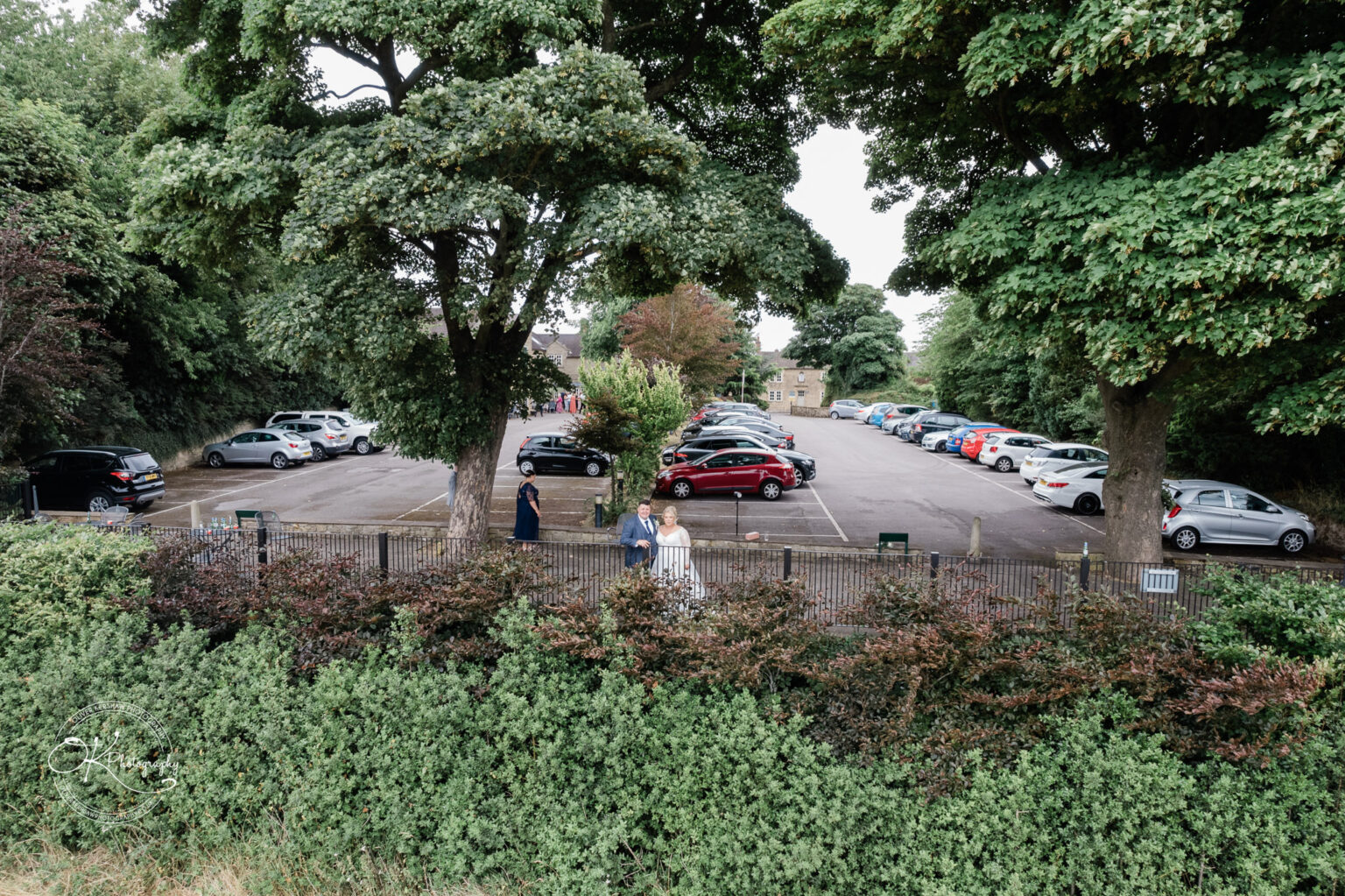 Santos Higham Farm Wedding Photography A car park surrounded by greenery and trees, with several people walking and cars parked.