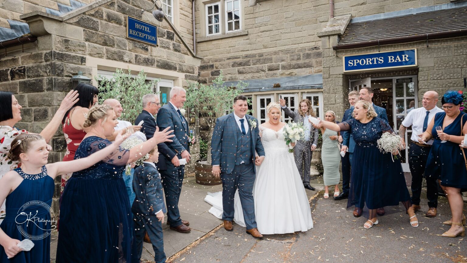 Santos Higham Farm Wedding Photography Wedding couple walking outside a stone building, surrounded by guests throwing confetti.
