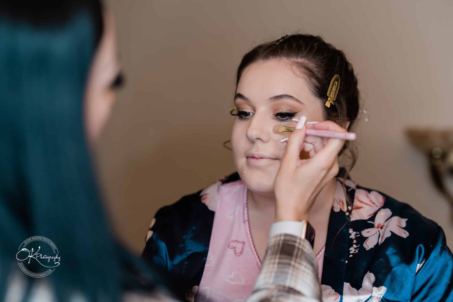 Santos Higham Farm Wedding Photography A person having makeup applied with a brush, wearing a dark floral robe and light pink shirt.