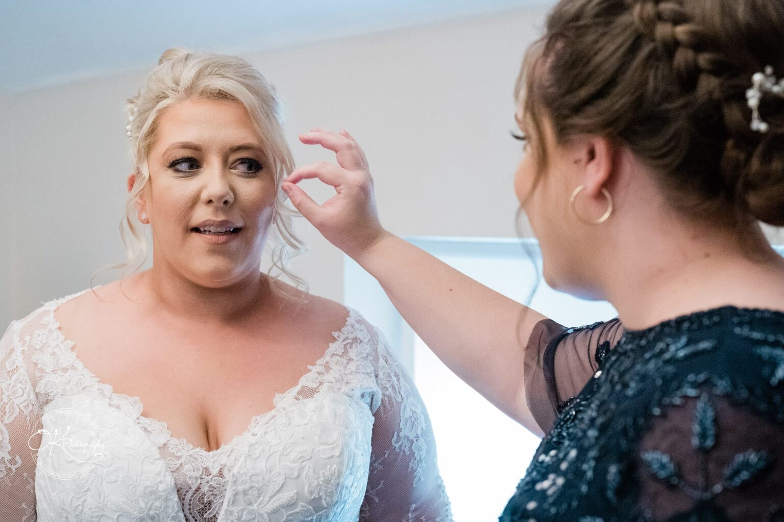 Santos Higham Farm Wedding Photography A bride in a white lace wedding dress is having her hair adjusted by a woman in a dark dress.