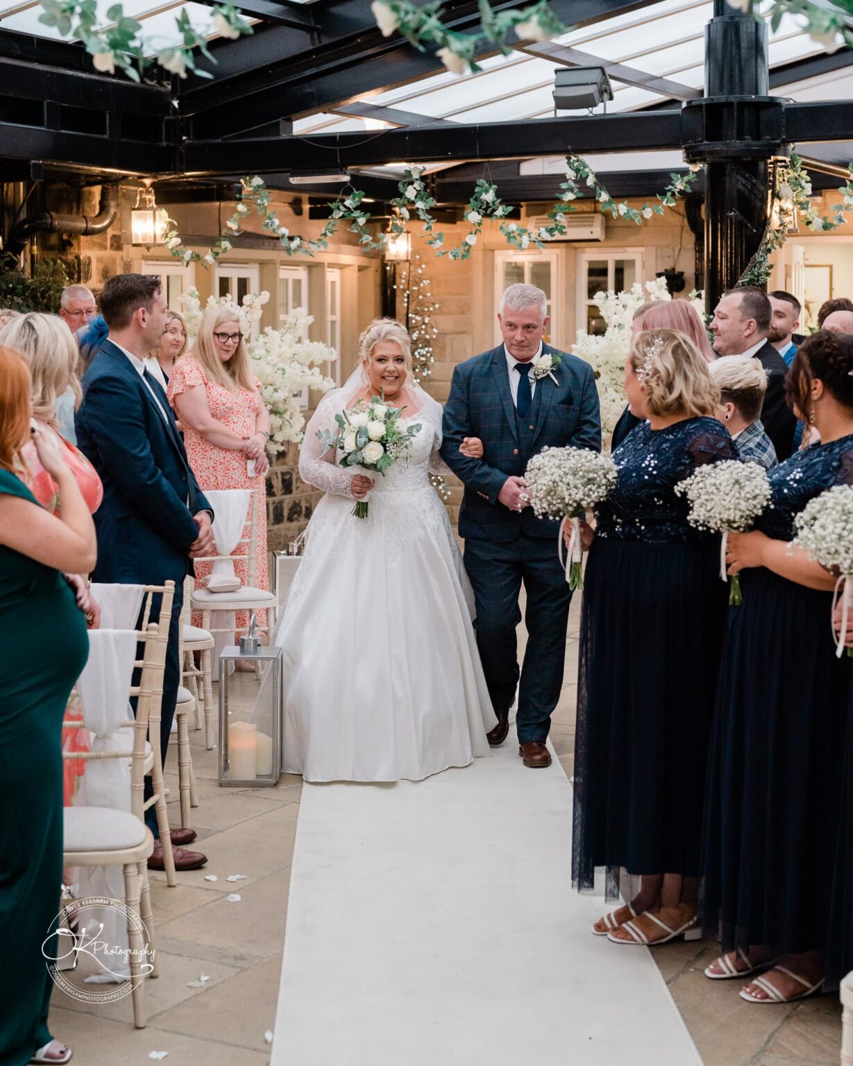 Santos Higham Farm Wedding Photography Bride walking down the aisle with her father at a wedding ceremony, with guests looking on and bridesmaids holding bouquets.