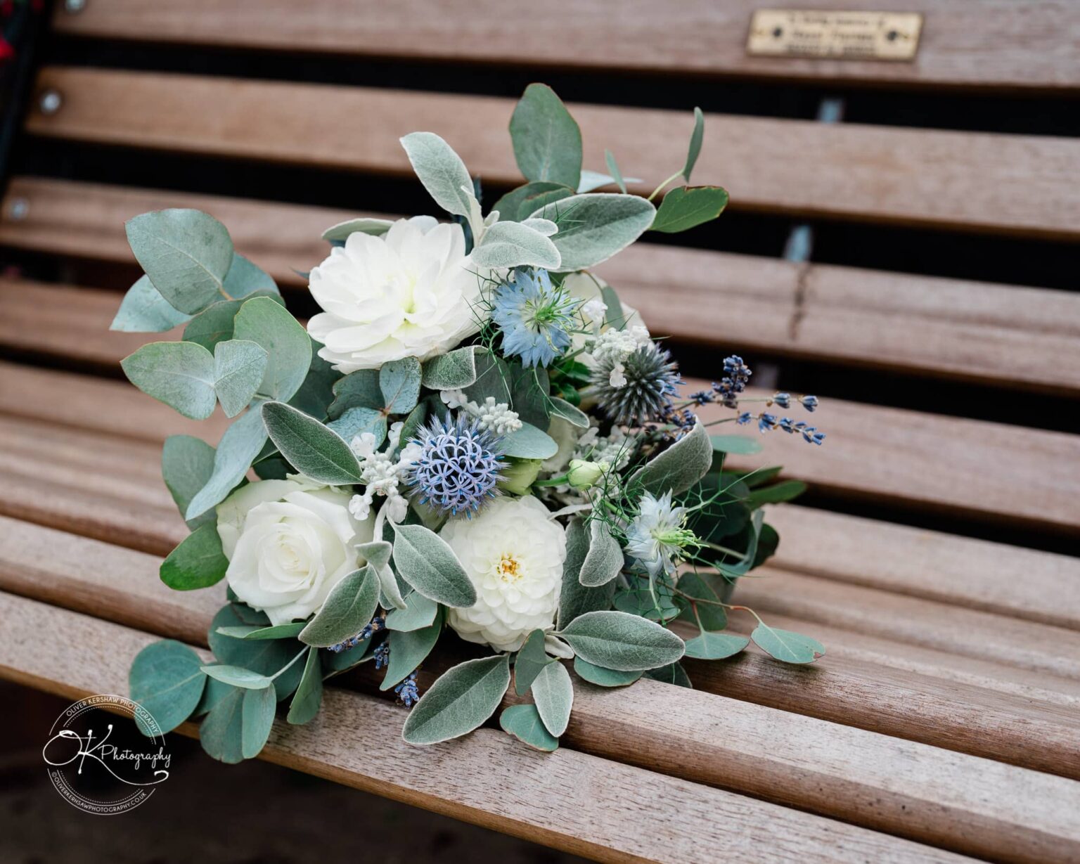 Shearsby Bath Wedding Photography A floral bouquet consisting of white and blue flowers with green leaves, placed on a wooden bench.