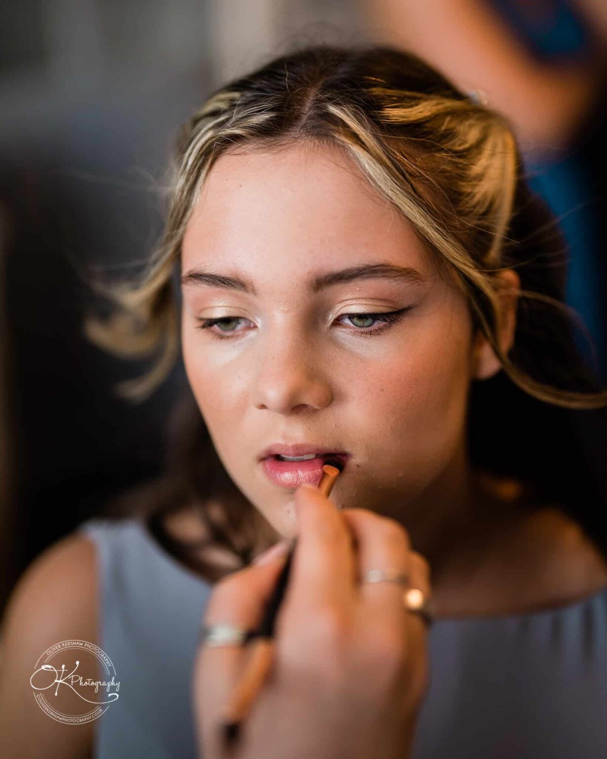 Shearsby Bath Wedding Photography Young woman having her makeup done, with focus on lips being applied a brush.