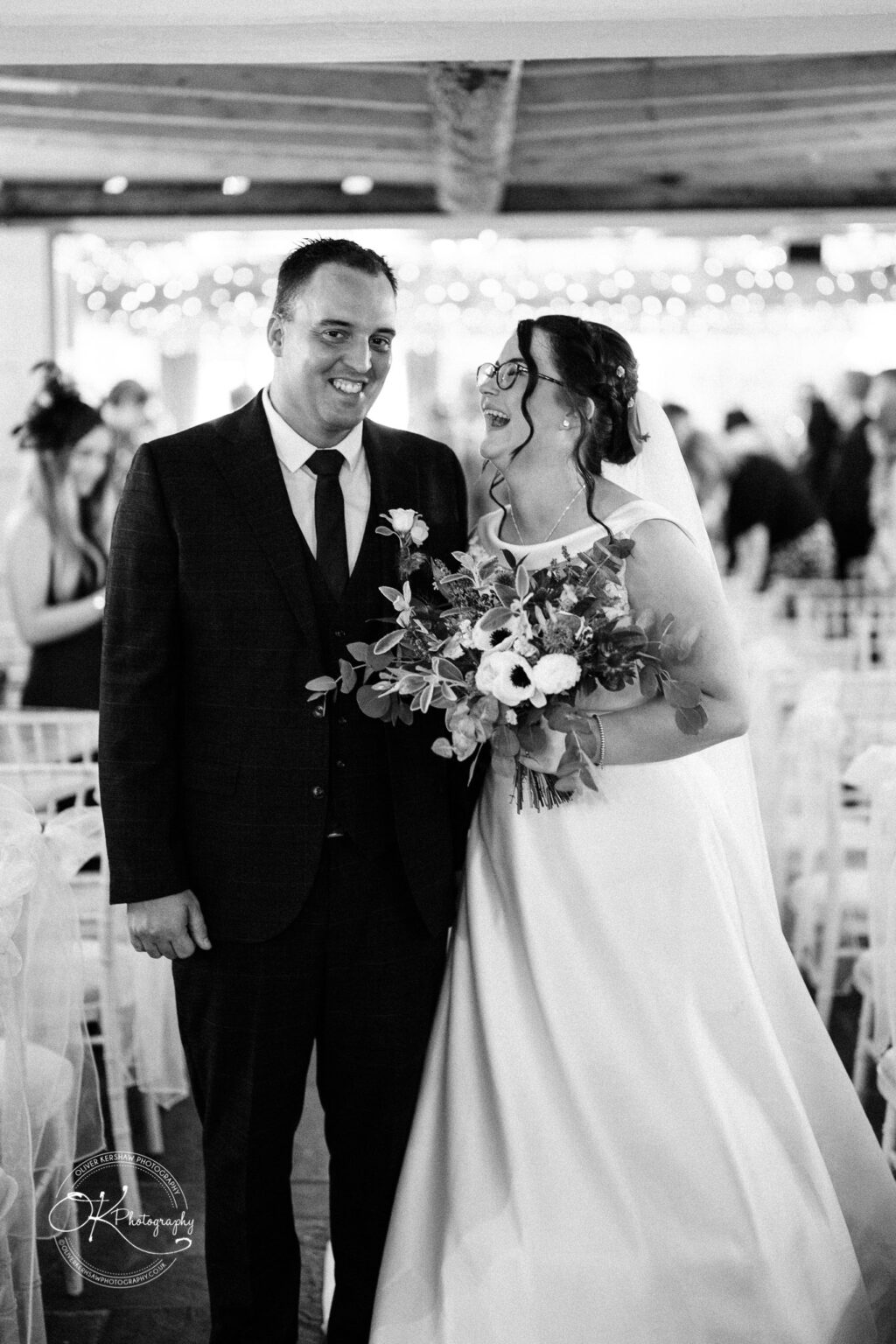 Shearsby Bath Wedding Photography A bride and groom smiling at each other during their wedding, with the bride holding a bouquet and wearing a veil, and the groom dressed in a suit.