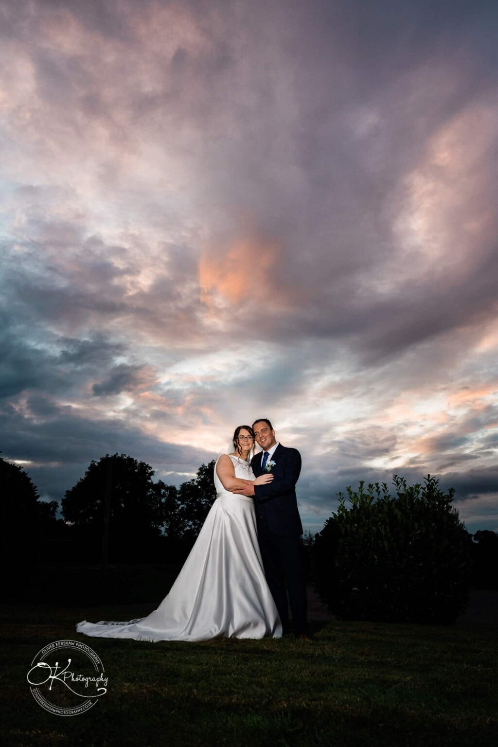 Shearsby Bath Wedding Photography Bride and groom standing together outdoors with a dramatic, colourful evening sky in the background.