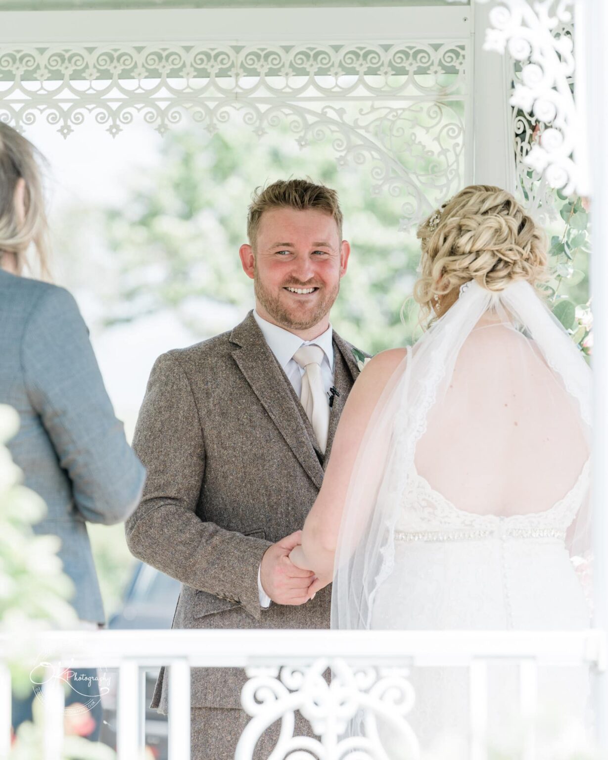 Bride and groom holding hands during their wedding ceremony under a decorative white gazebo.