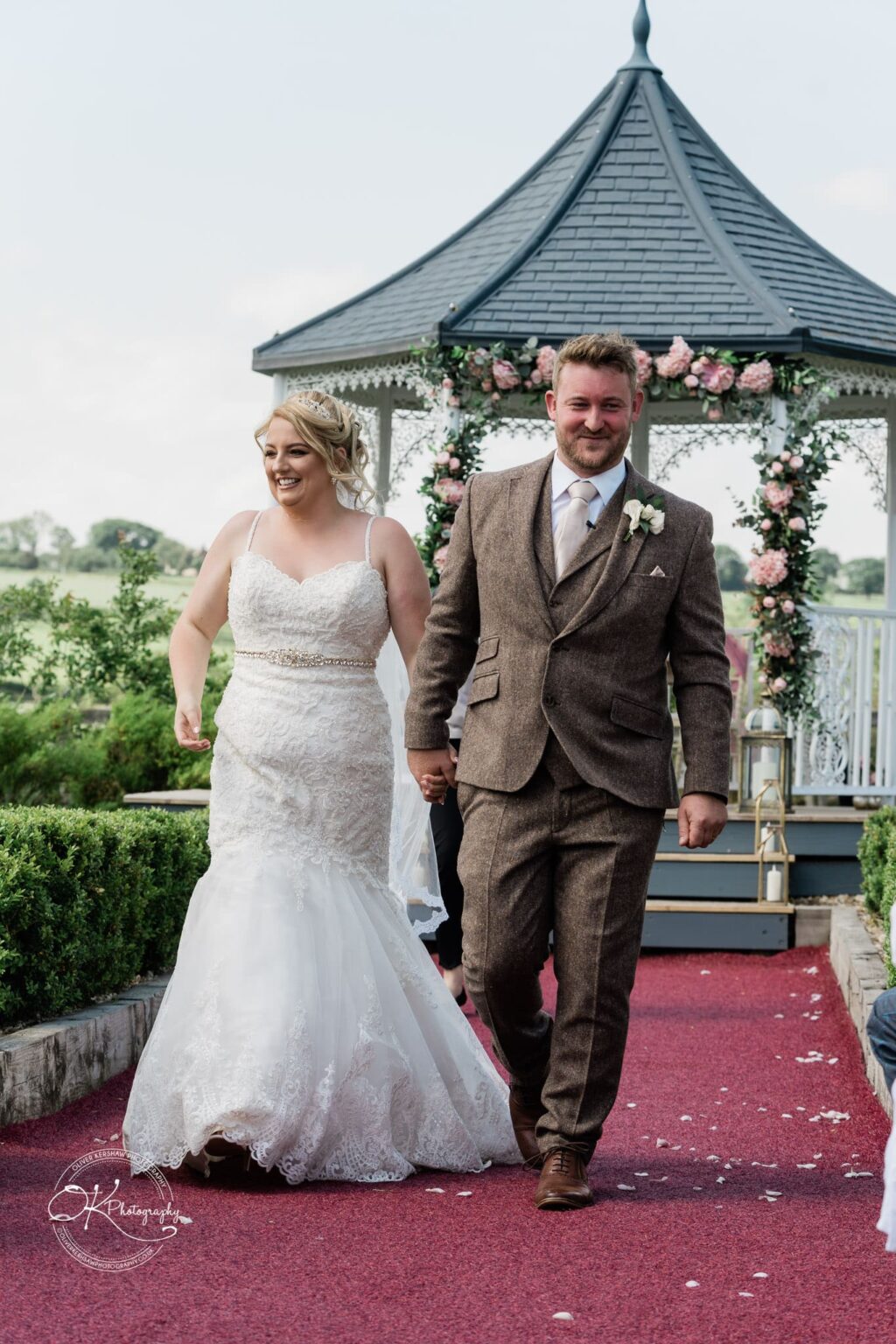 Bride and groom walking down the aisle with a decorated gazebo in the background.
