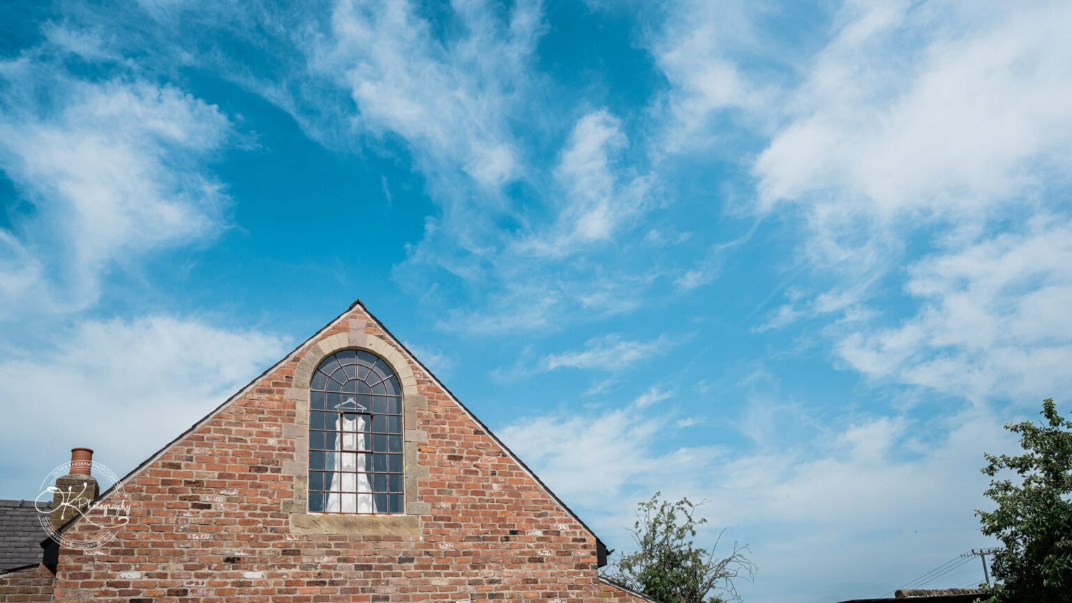 Brick building with arched window under a blue sky with scattered clouds.
