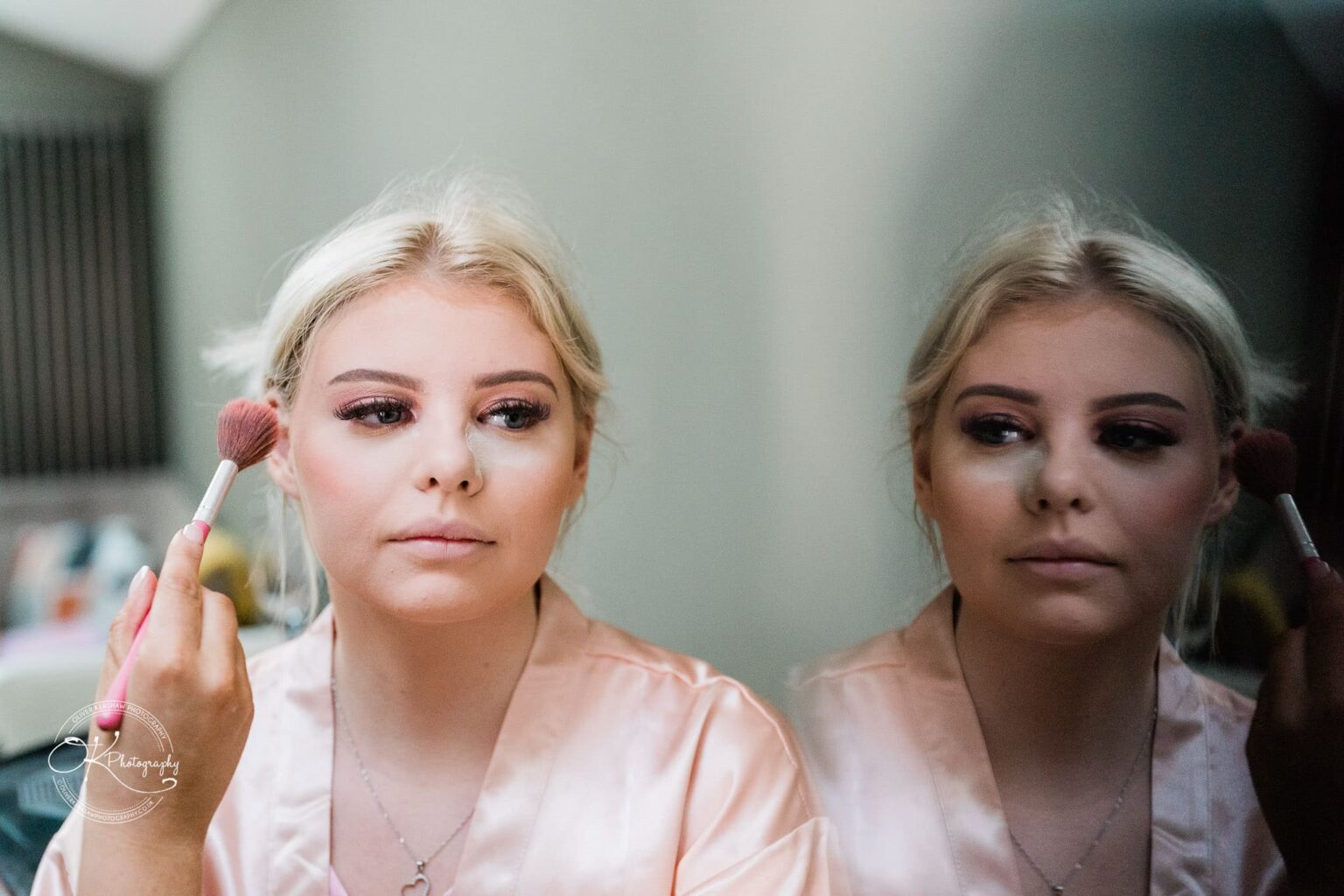 A woman applying makeup with a brush in front of a mirror.