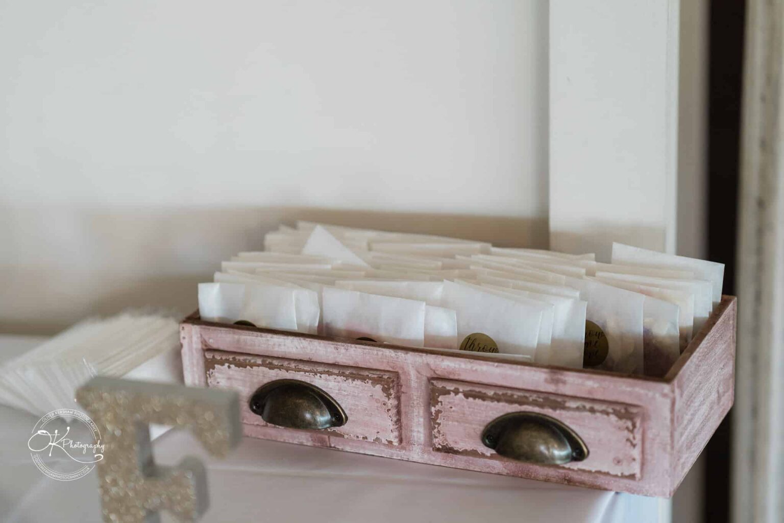 A wooden tray filled with small white paper bags, each sealed with a round sticker, placed on a white tablecloth.