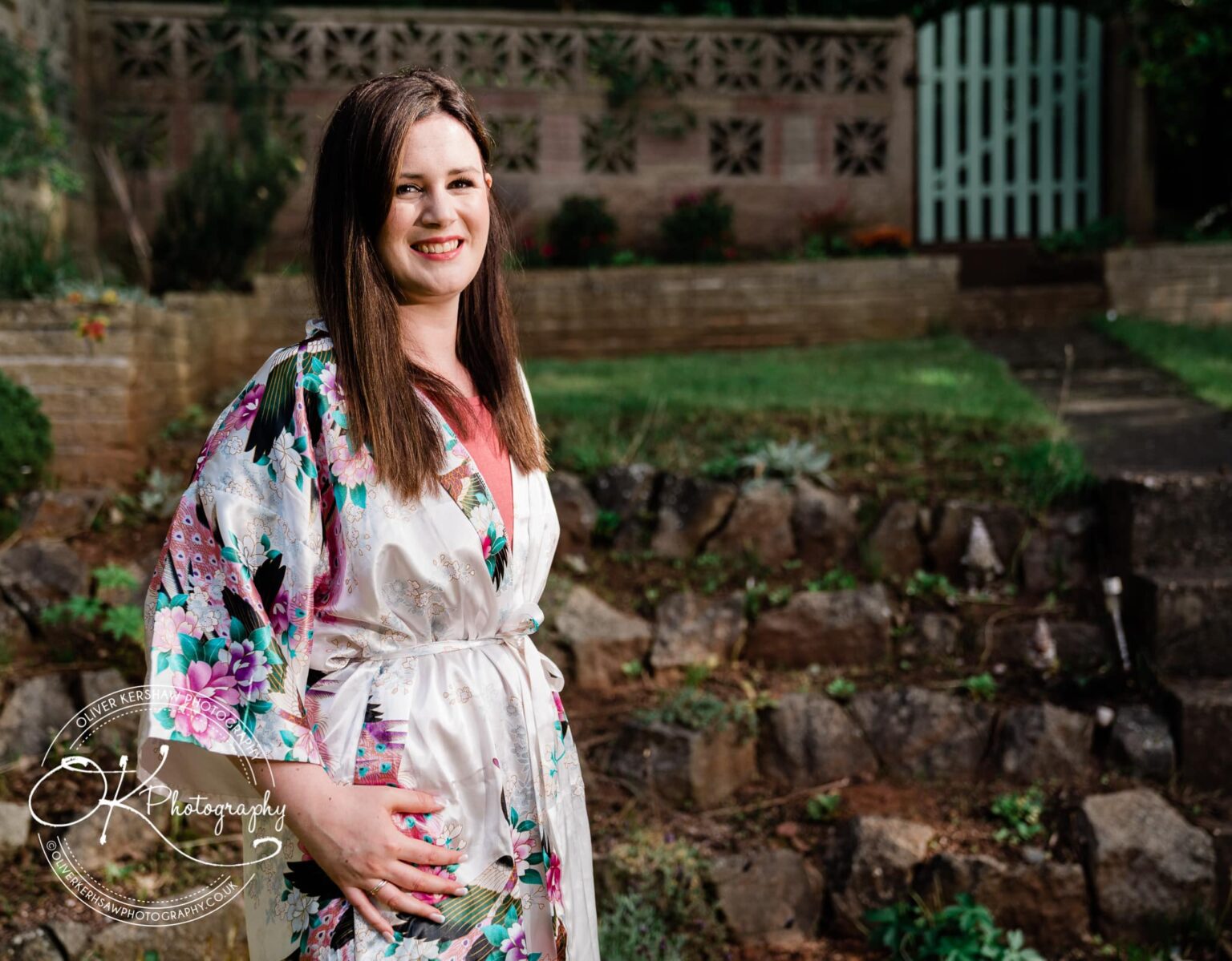 A woman in a floral robe smiling in an outdoor garden setting.