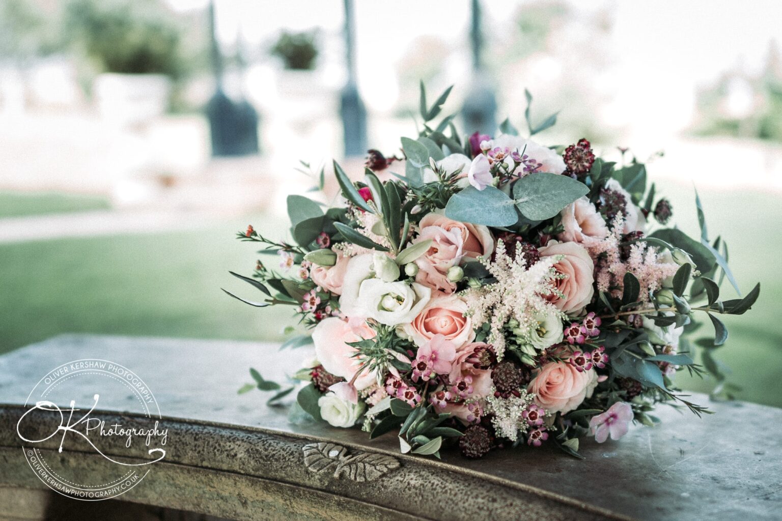 A bridal bouquet made of pink roses, white flowers, and green foliage rests on a stone bench with a butterfly engraving.